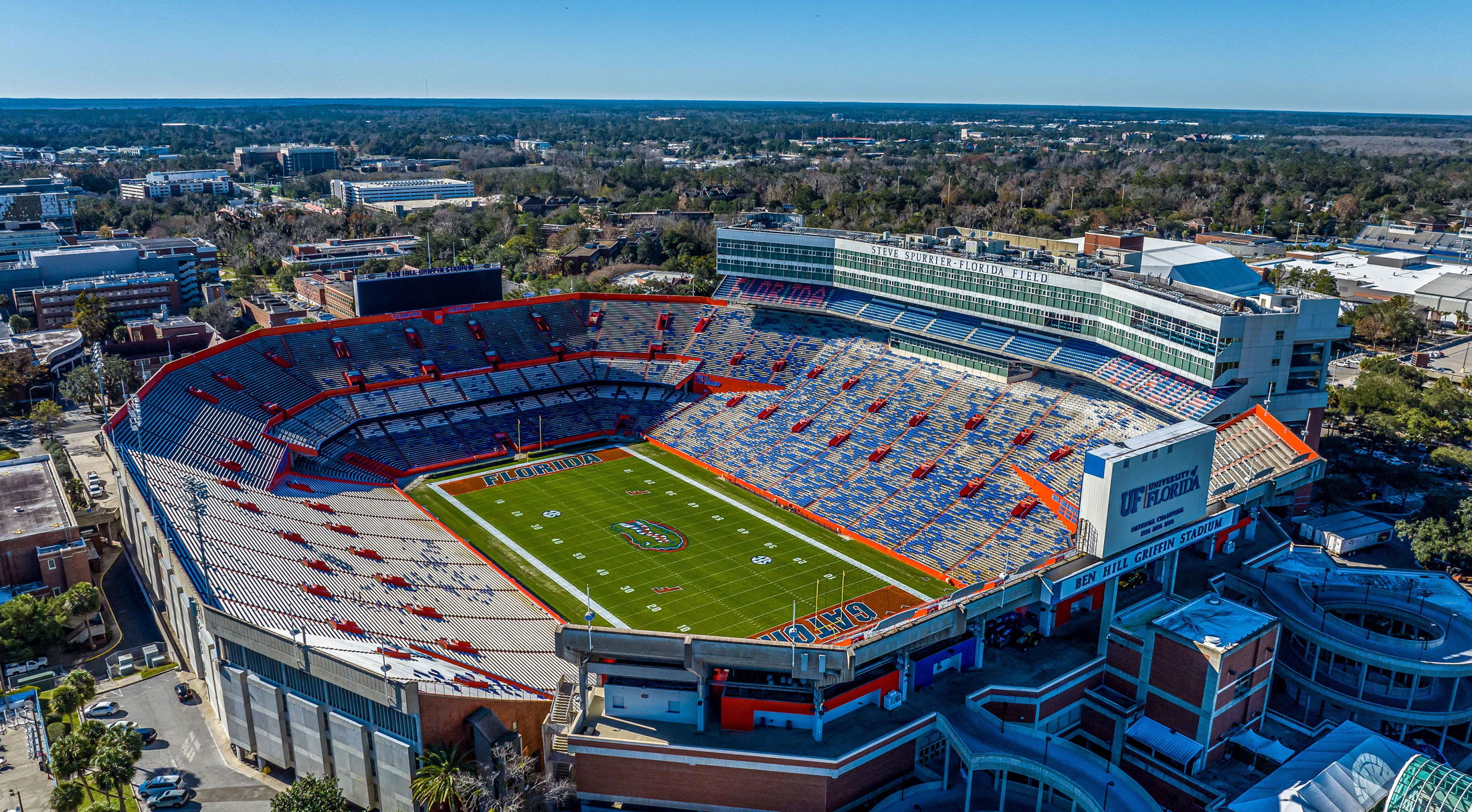 Aerial view of Ben Hill Griffin Stadium, home to the University of Florida Gators, featuring empty bleachers and a vibrant green football field.