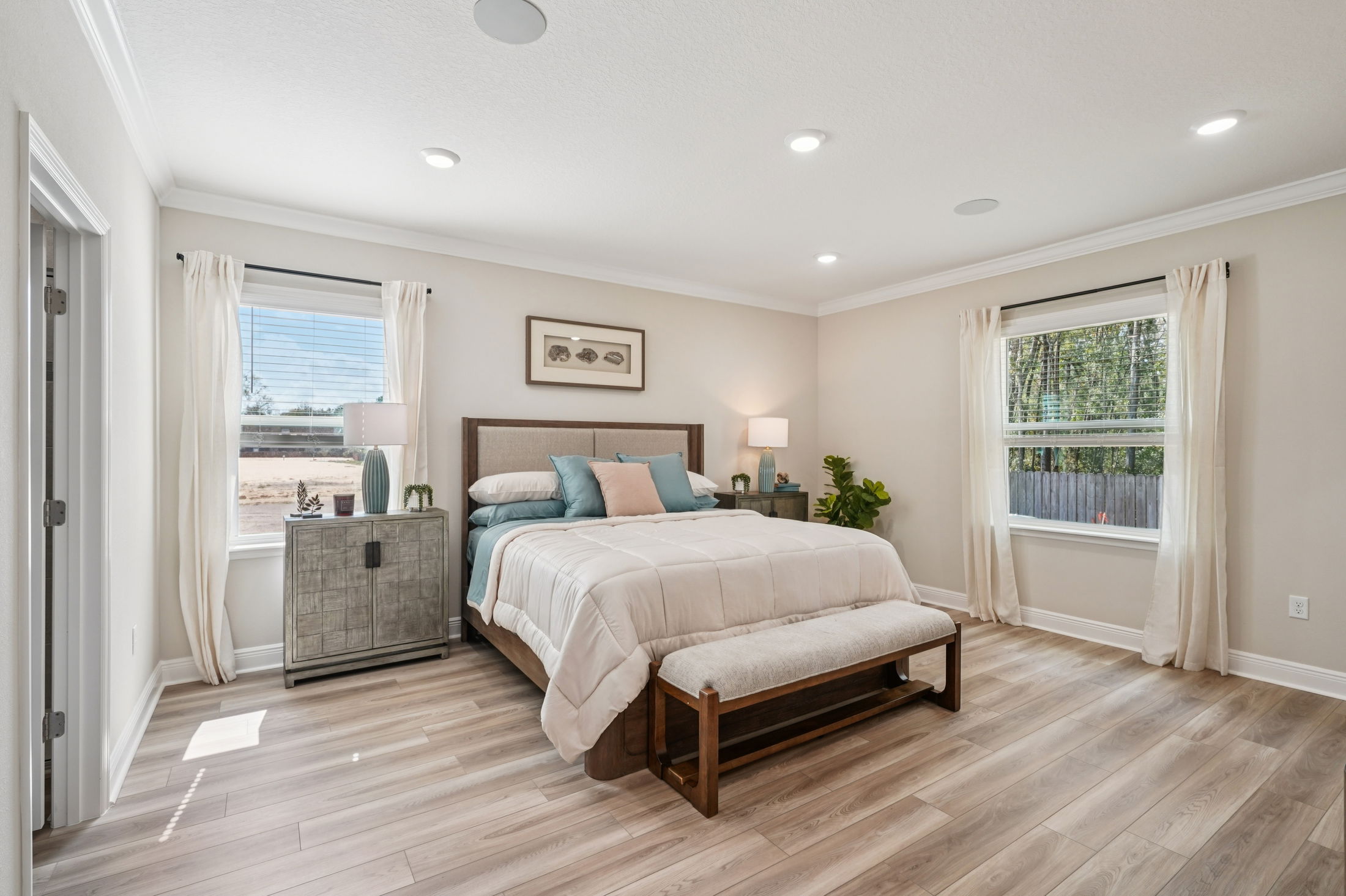 Modern bedroom interior featuring a cozy bed with decorative pillows, stylish bedside tables, natural lighting from windows, and wooden flooring.