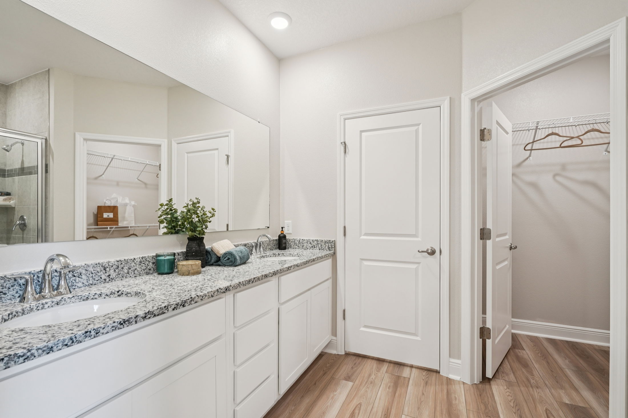 Modern bathroom design featuring a spacious vanity with granite countertops, mirror, and wooden flooring.