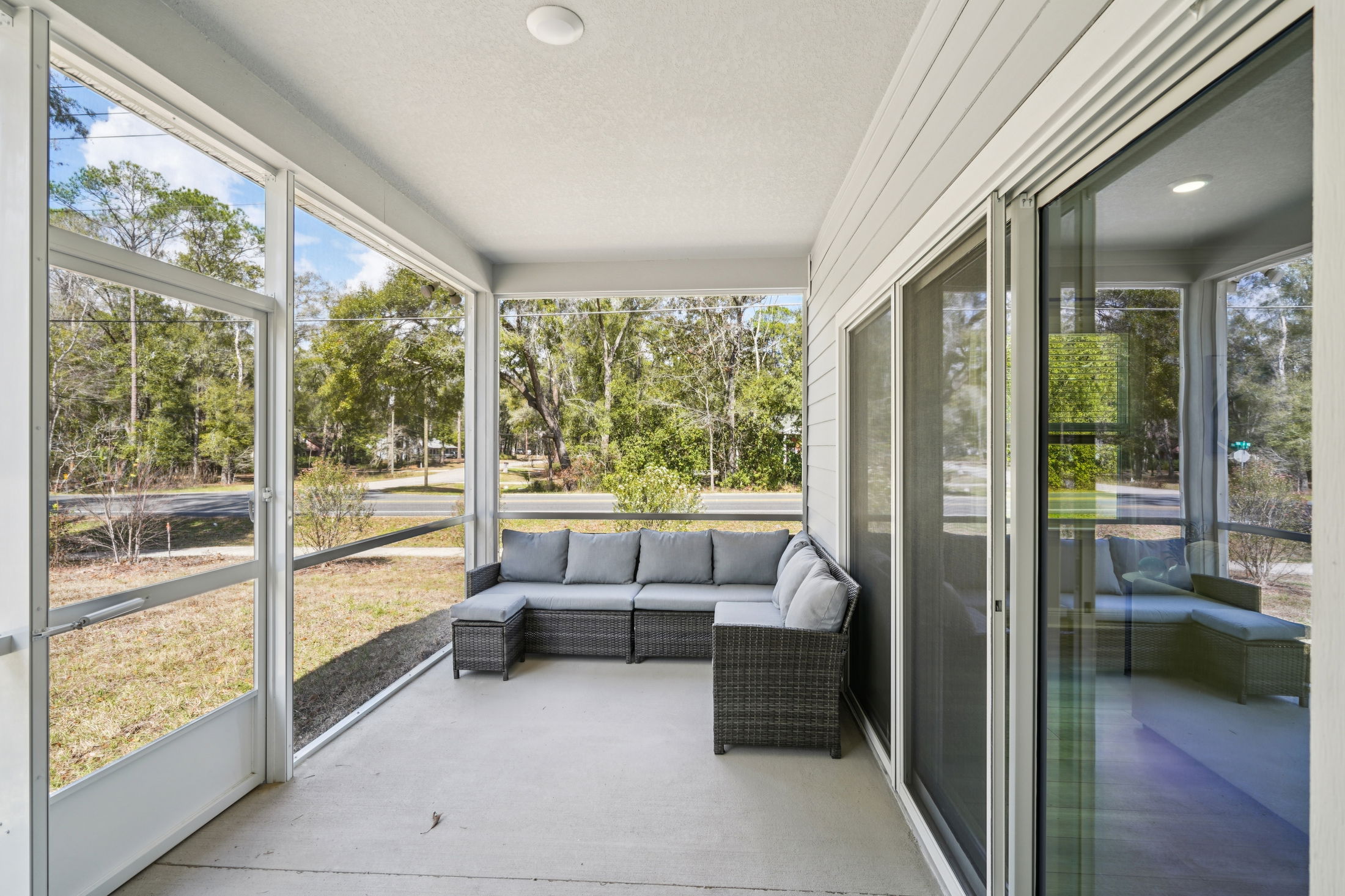 A cozy screened-in porch featuring comfortable gray seating and a view of the surrounding greenery.