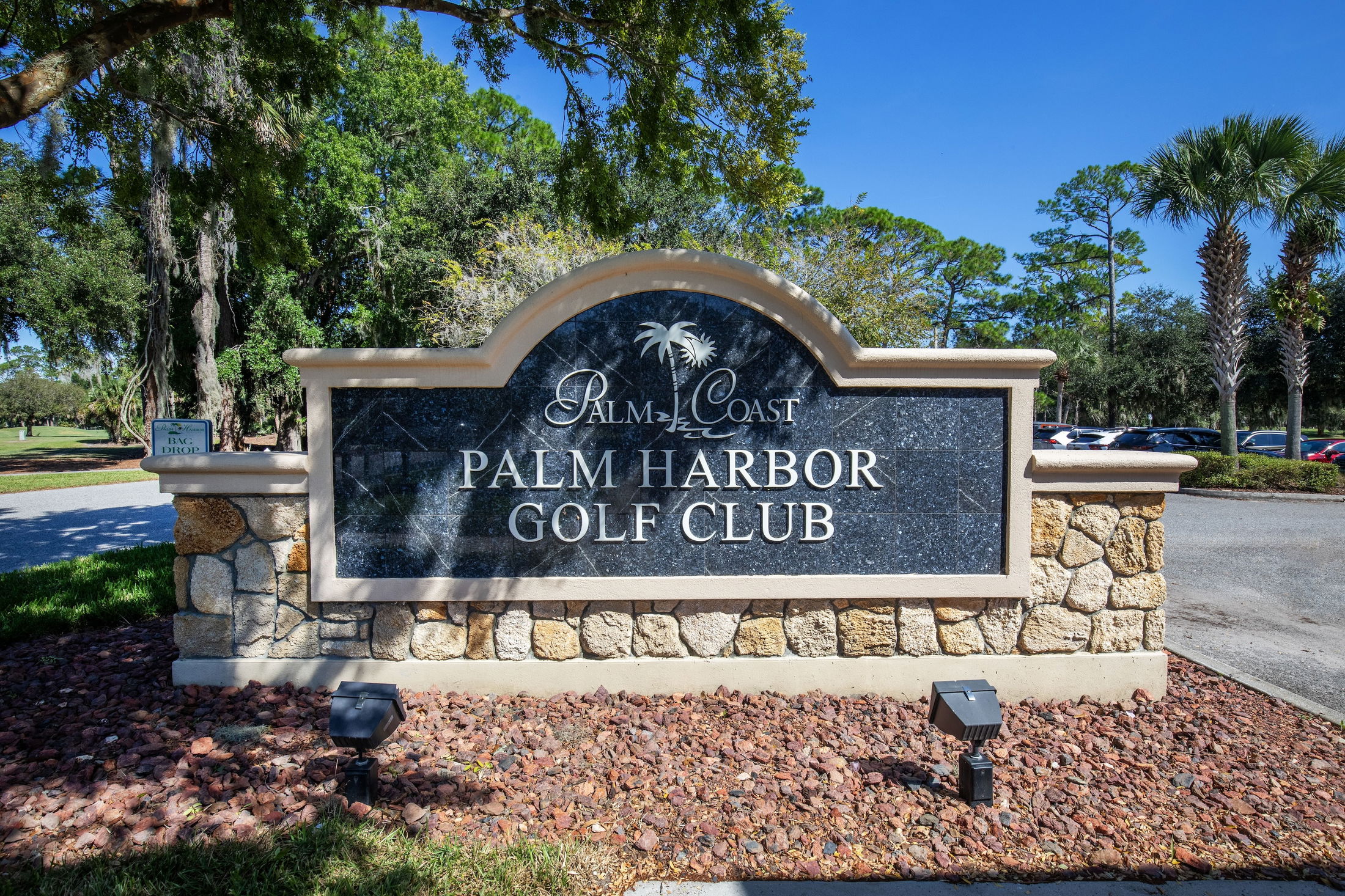Sign for Palm Harbor Golf Club in Palm Coast, surrounded by trees and a sunny blue sky.