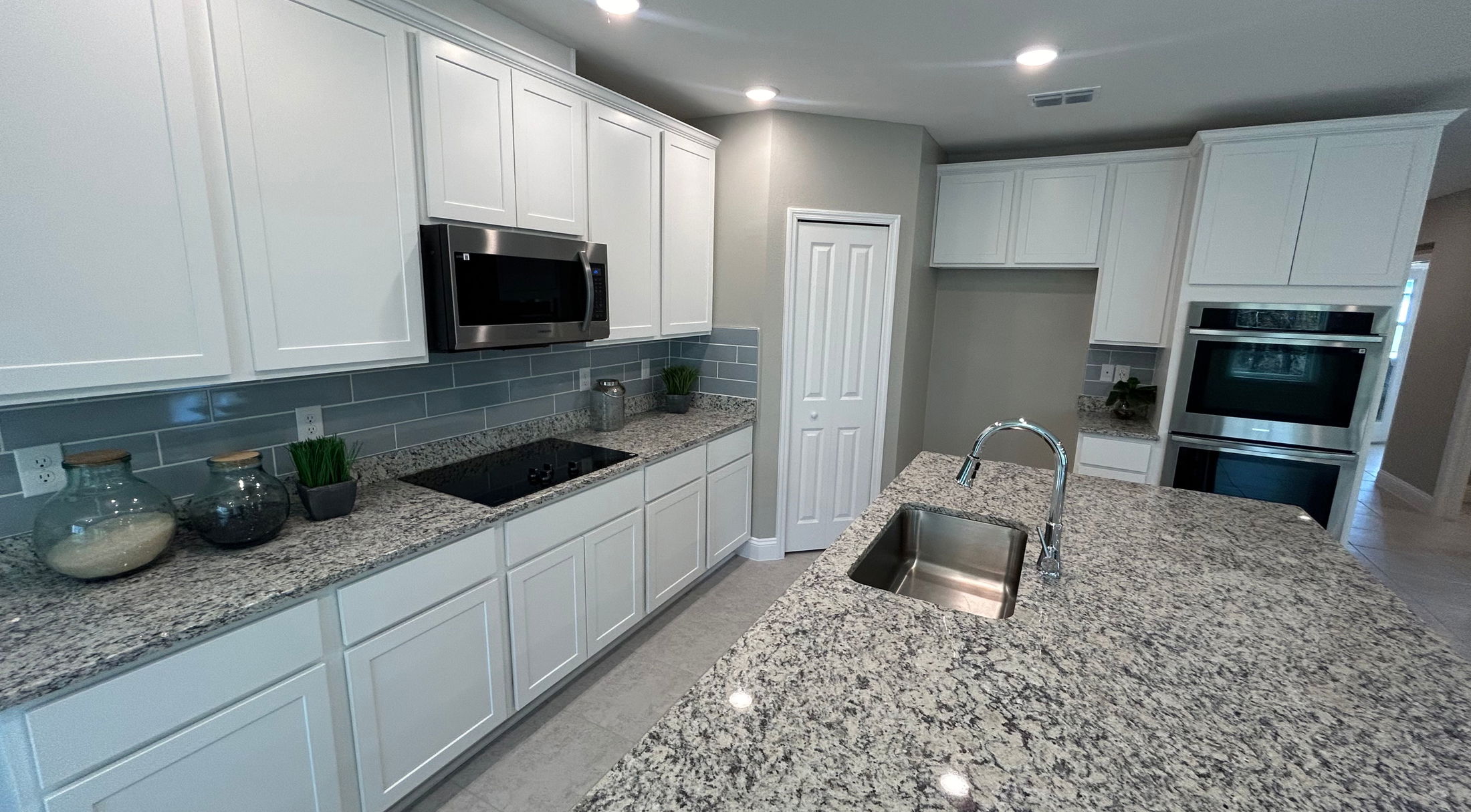 Modern kitchen with granite countertops, white cabinets, built-in stainless steel appliances, and a sleek island sink.