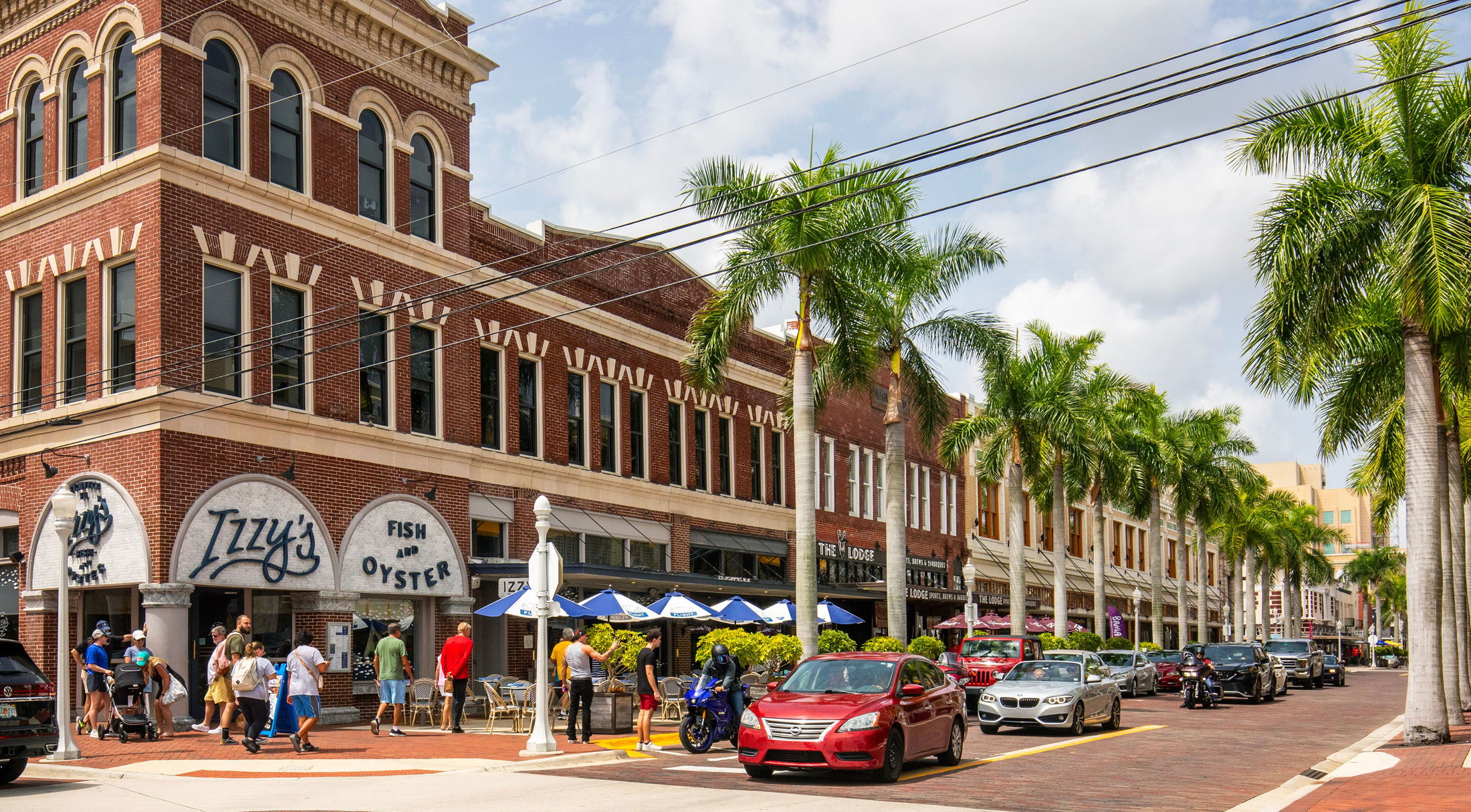 Bustling street view in Fort Myers, Florida, featuring historic red-brick buildings, palm trees, and outdoor dining.