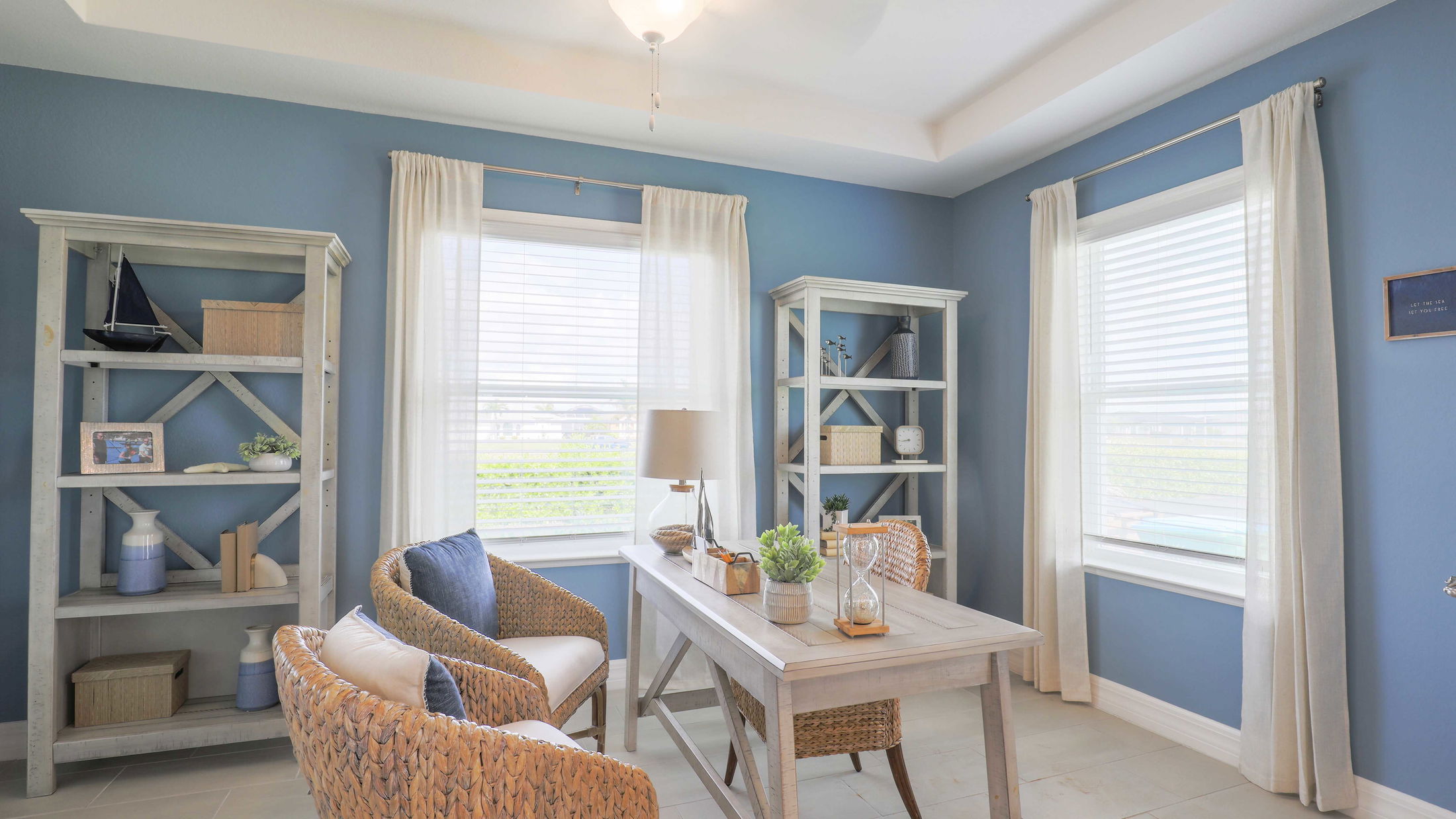 Coastal-themed home office with blue walls, wicker chairs, and decorative shelving.