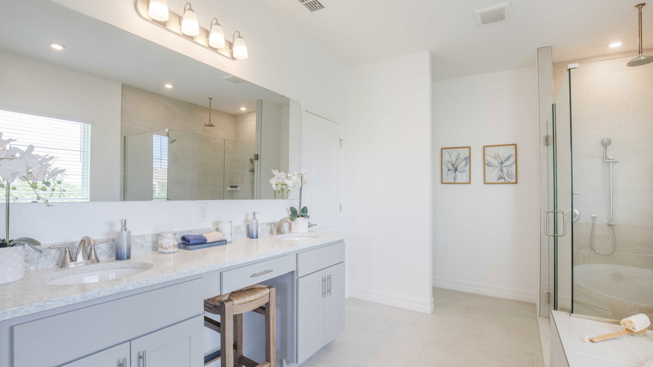Modern bathroom with a glass-enclosed shower, dual sinks on a marble countertop, and contemporary decor elements.