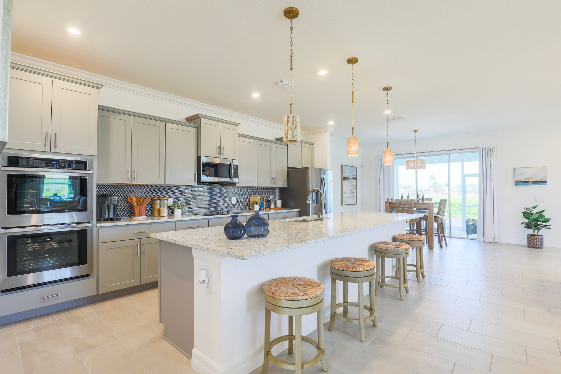 Modern kitchen interior with beige cabinets, marble countertops, barstools, and pendant lighting.