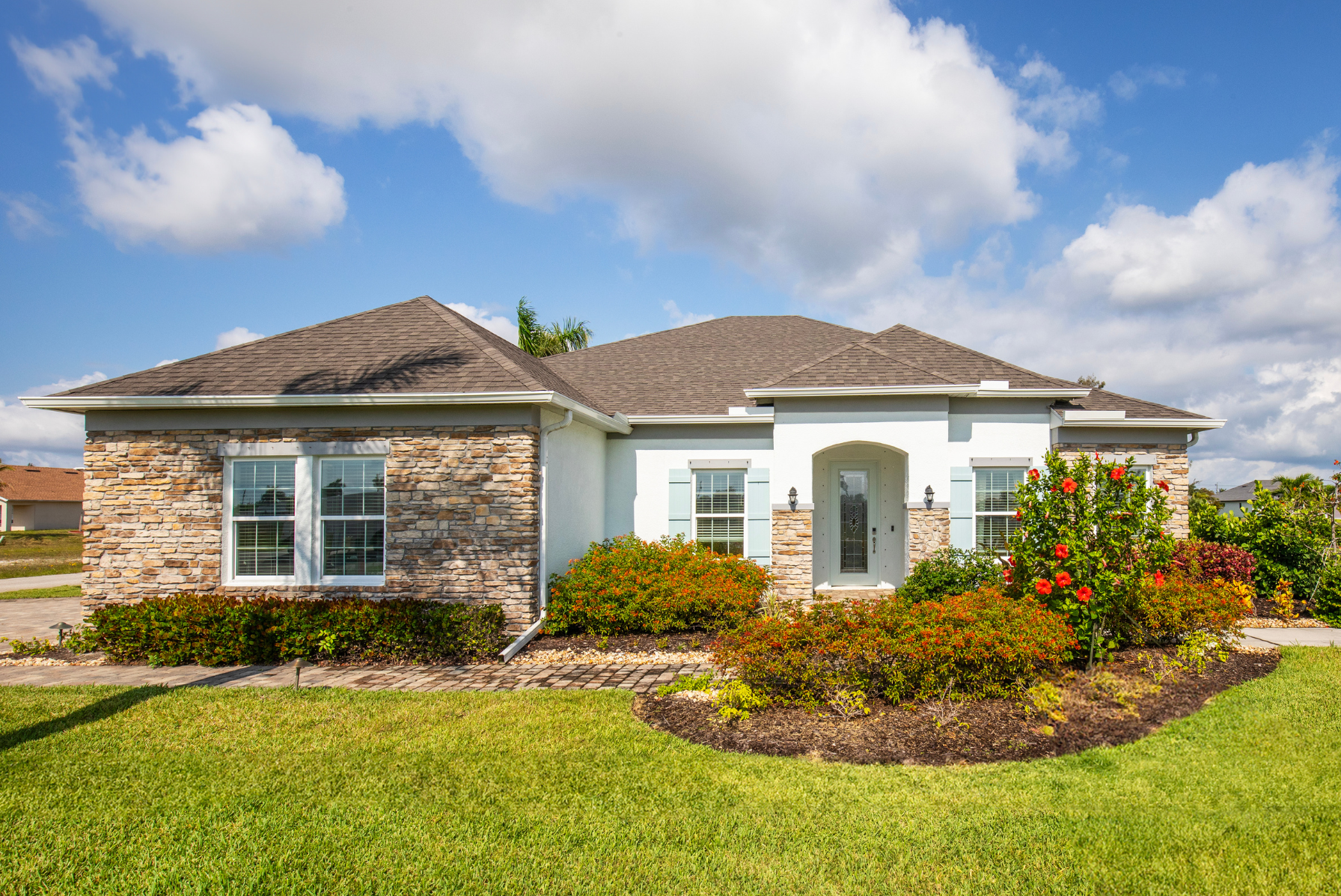Modern suburban home with stone facade, manicured lawn, and colorful garden under a clear blue sky.