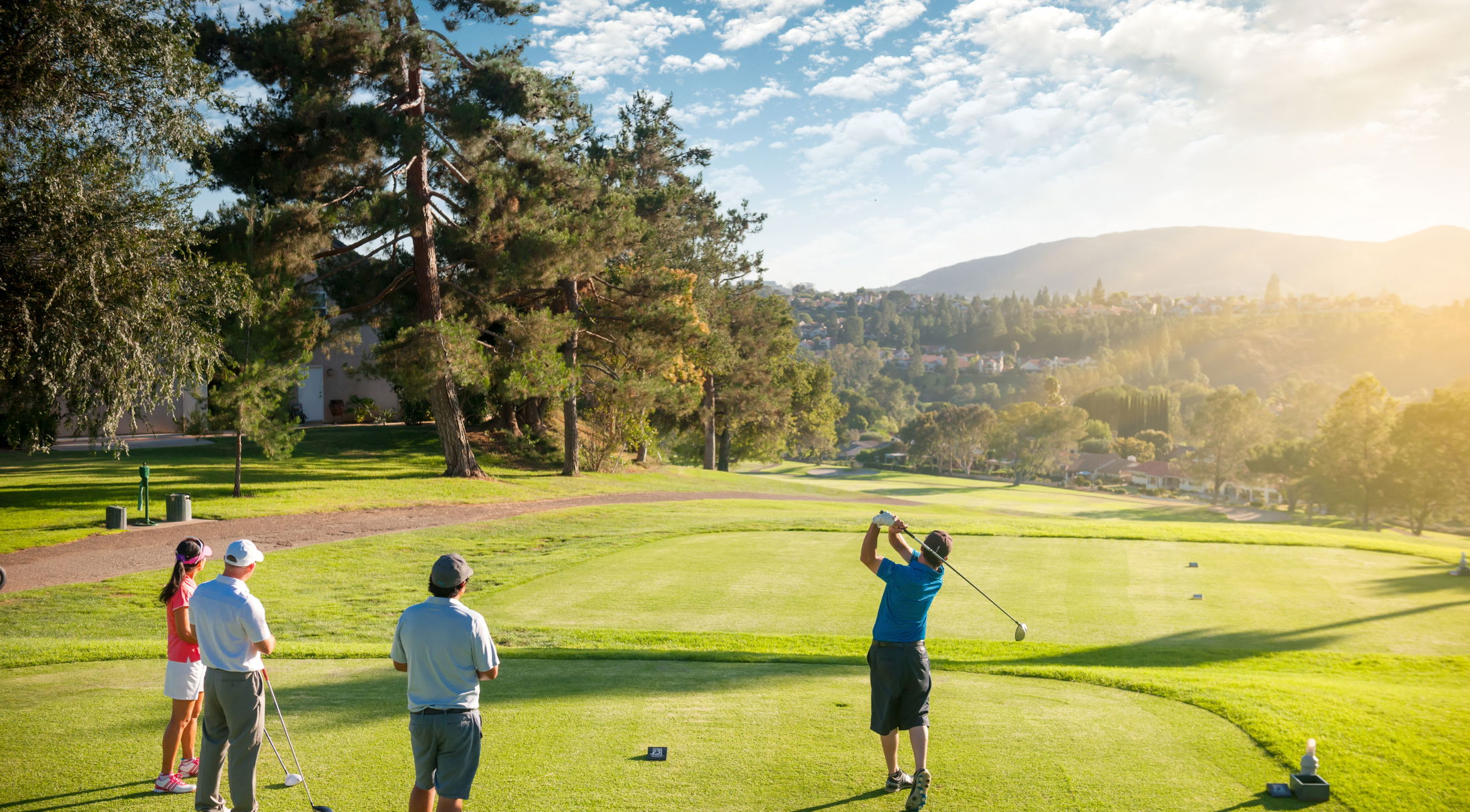 Golfers playing at a scenic course with a mountain backdrop under a bright, sunny sky.