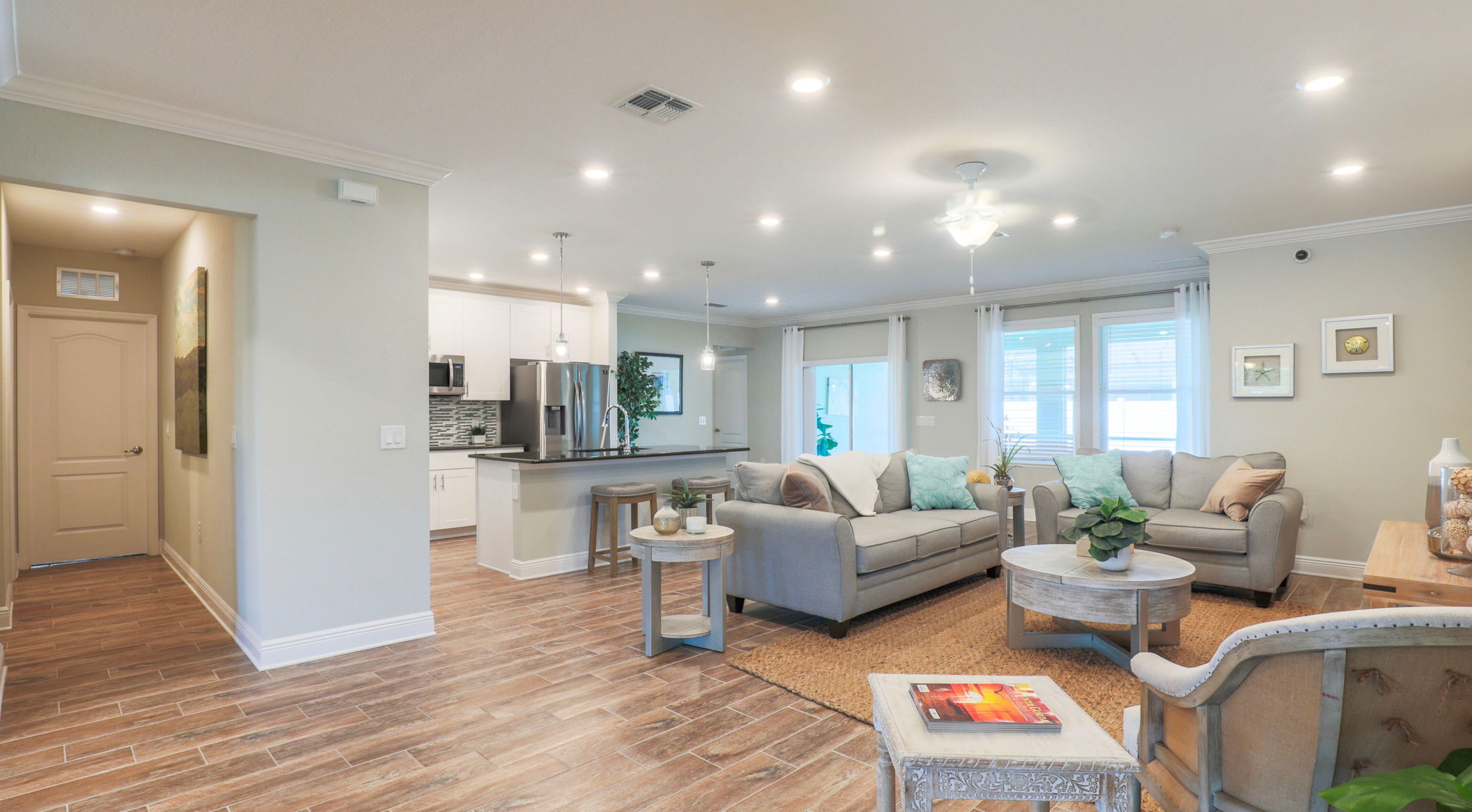 Modern open-concept living room with cozy gray furniture, wood flooring, and a sleek kitchen island.