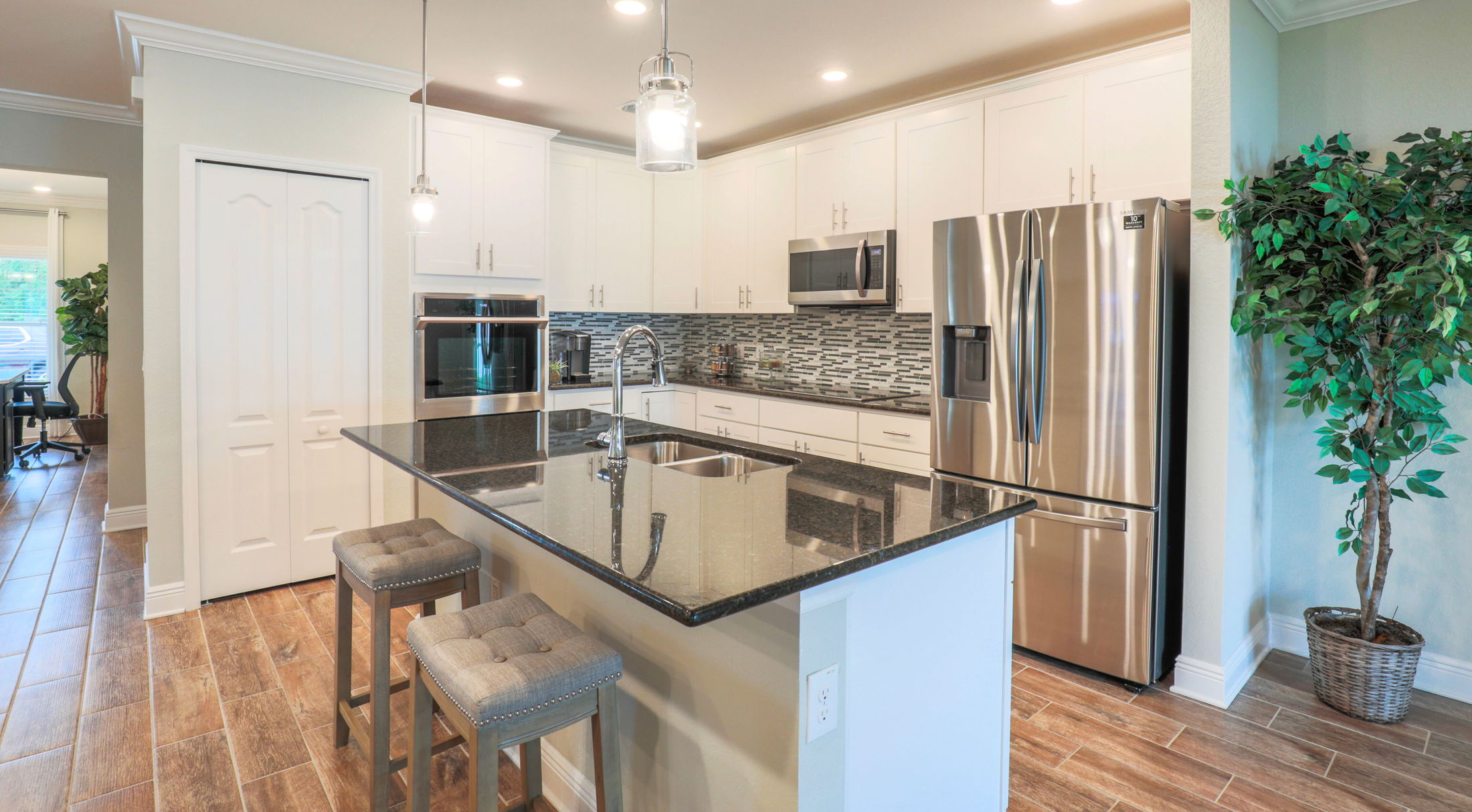 Modern kitchen with stainless steel appliances, white cabinetry, granite countertops, and a central island with stools.