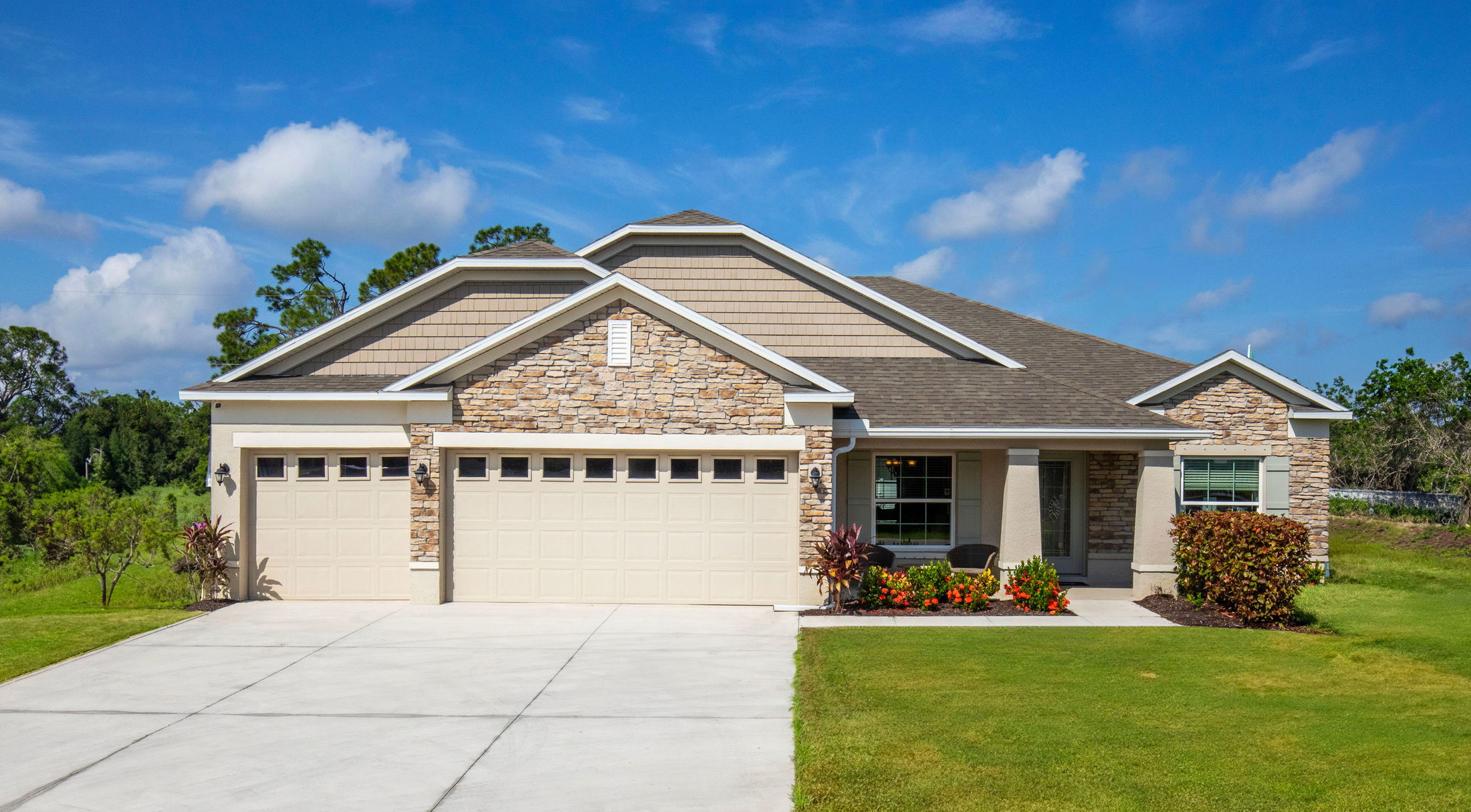 A modern suburban home with a stone facade, three-car garage, and landscaped yard under a clear blue sky.