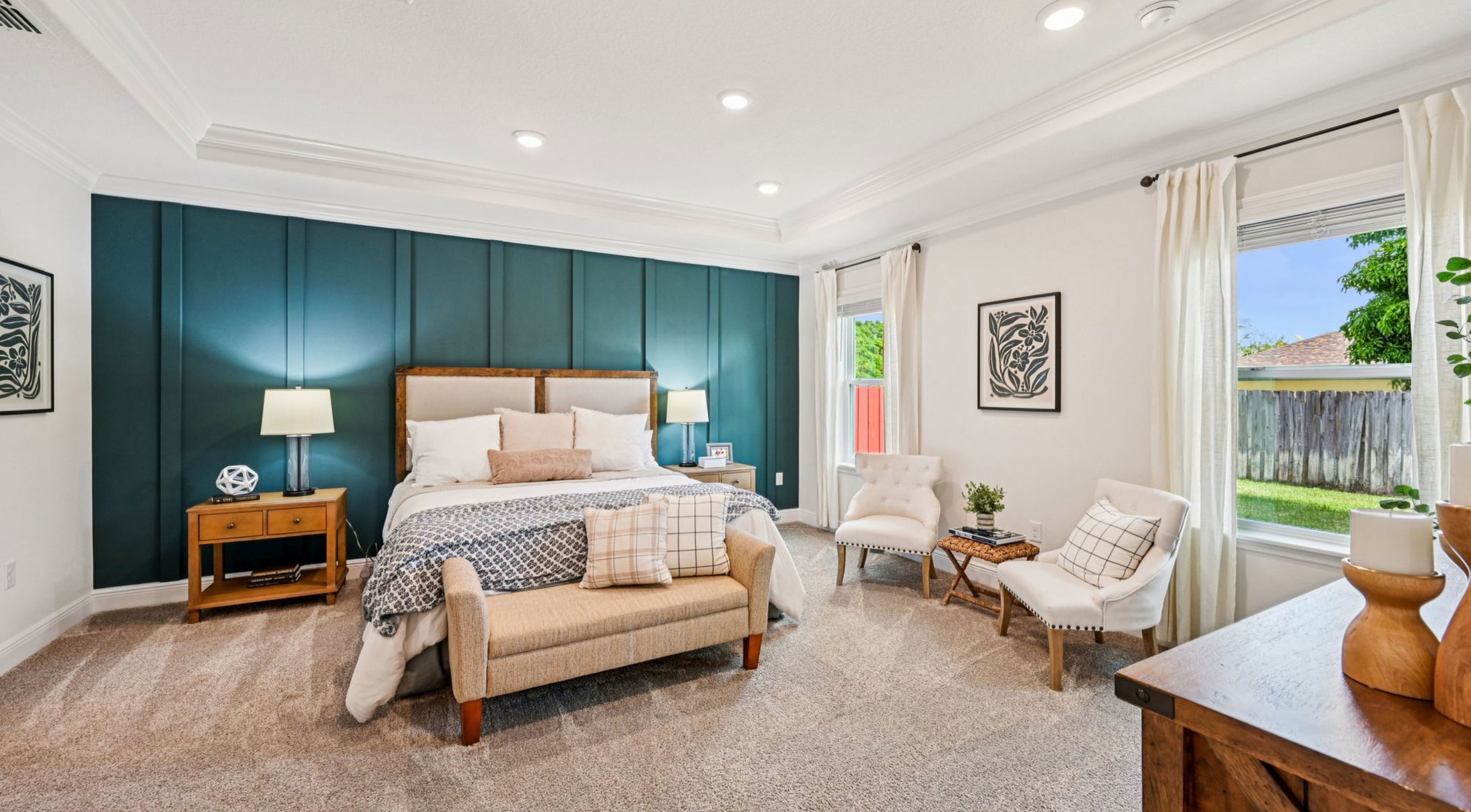 Contemporary bedroom with elegant decor featuring a teal accent wall, plush bedding, cozy seating area, and natural light from a large window.