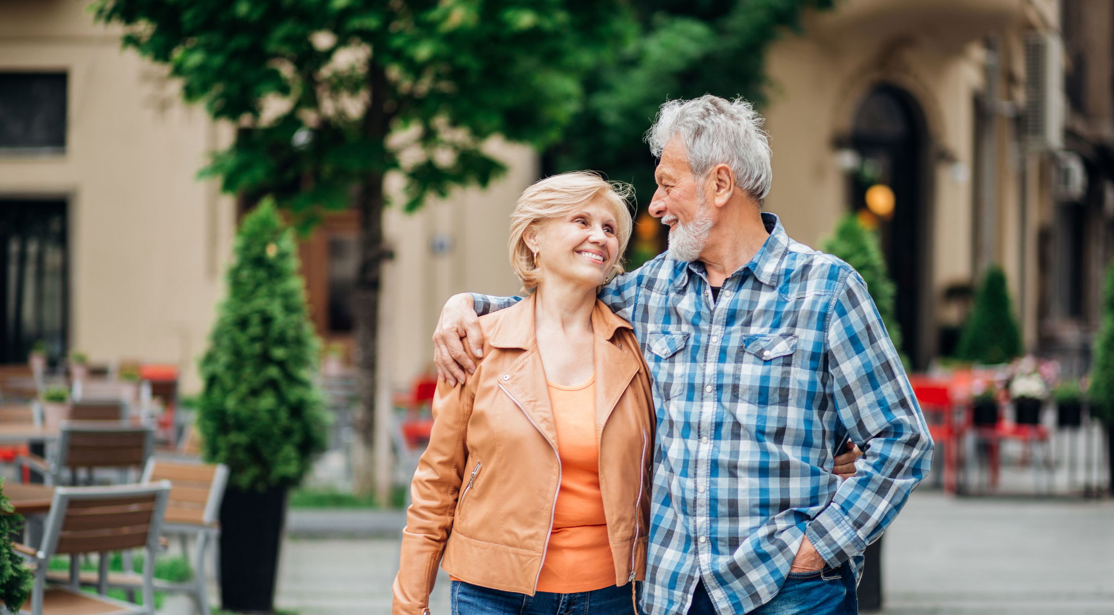 Elderly couple smiling and embracing while walking happily through a city street.