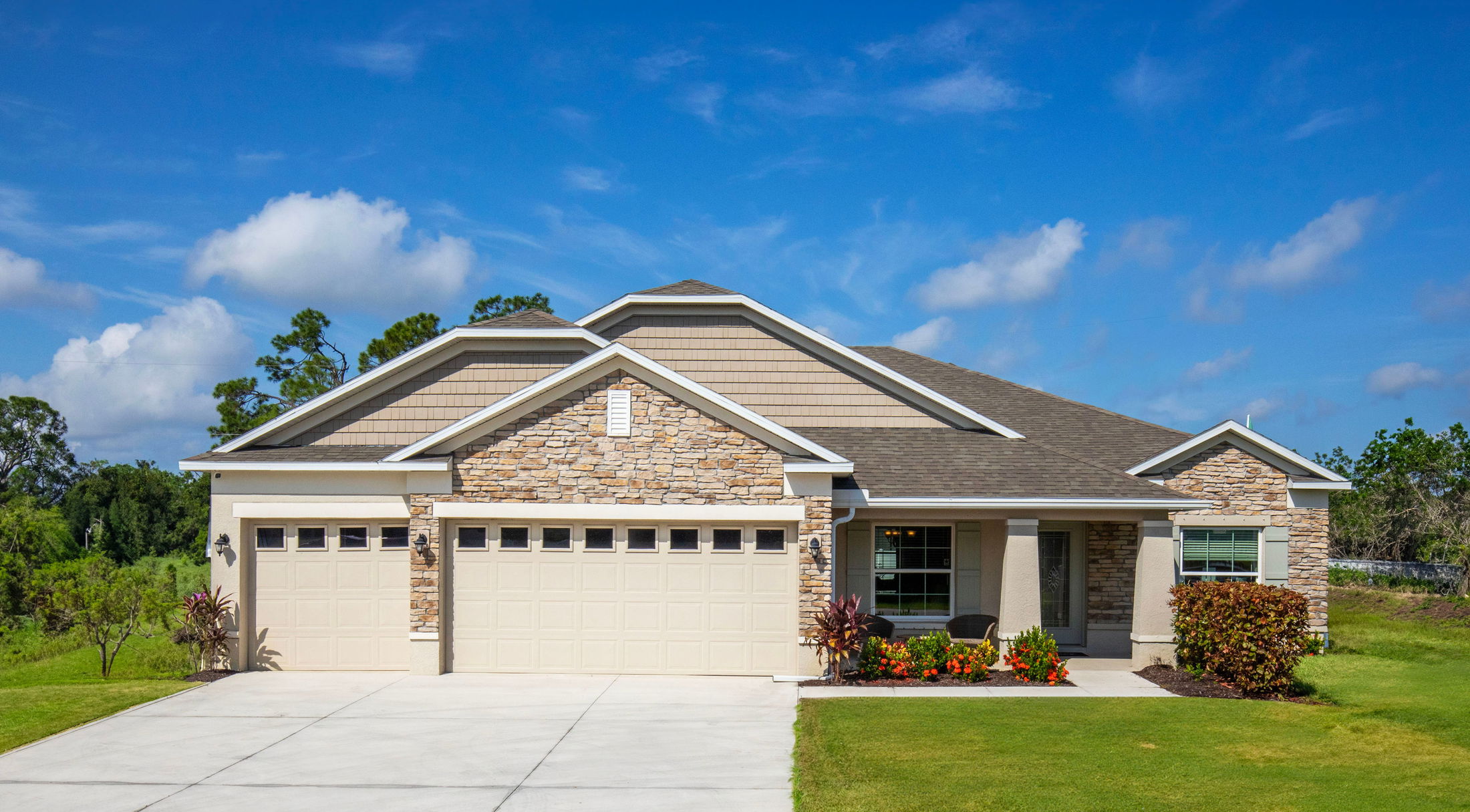 Modern single-story home with stone and siding exterior, featuring a three-car garage and manicured landscaping under a clear blue sky.