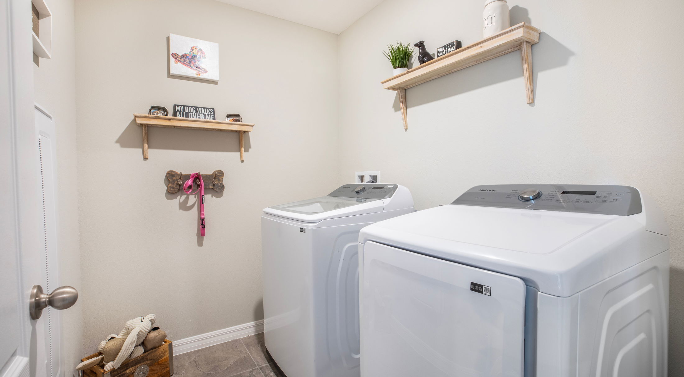 Modern laundry room with Samsung washer and dryer, pet-themed decor, and wooden shelves.