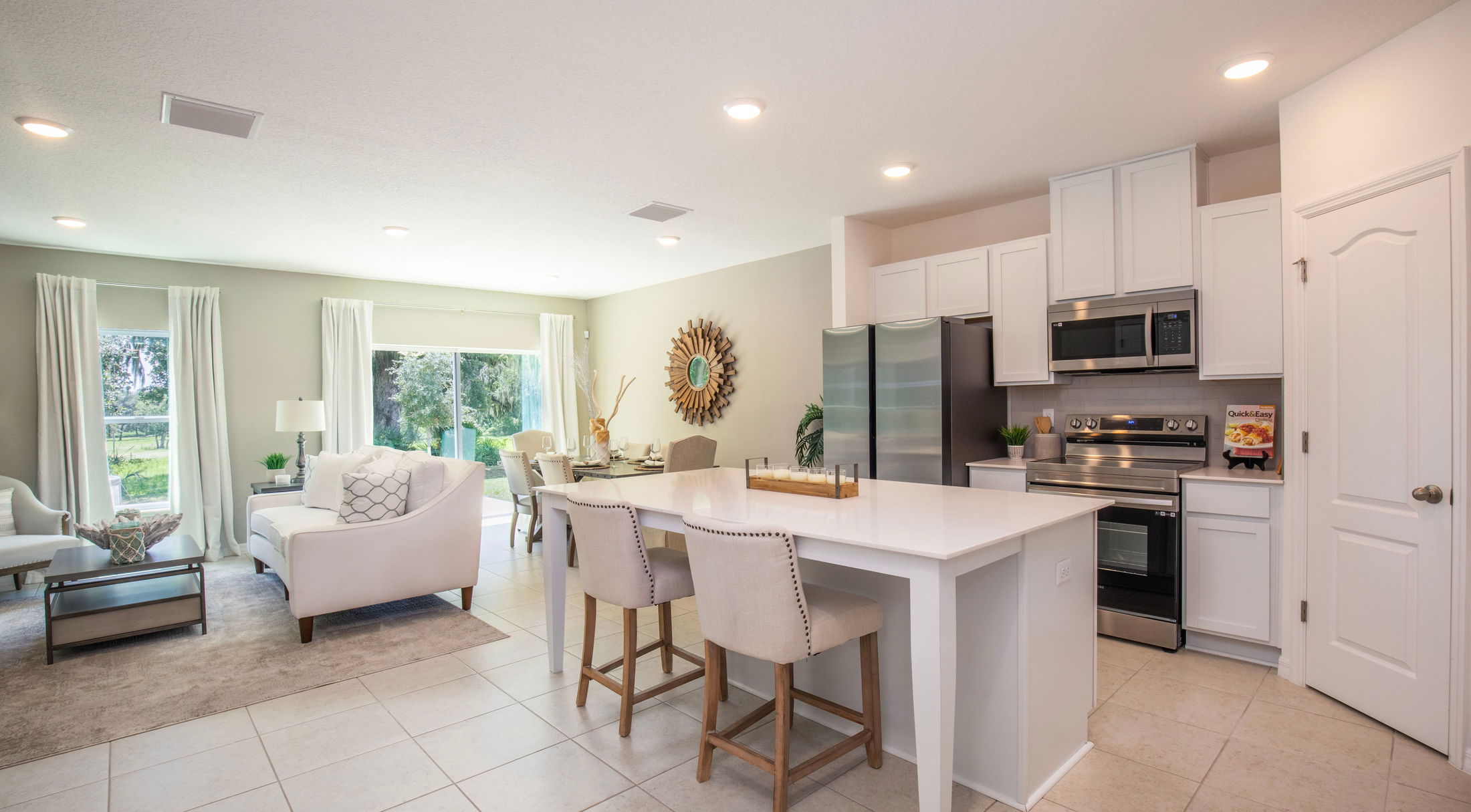 Modern open-plan kitchen and living room featuring a sleek white island, stainless steel appliances, and bright natural lighting.