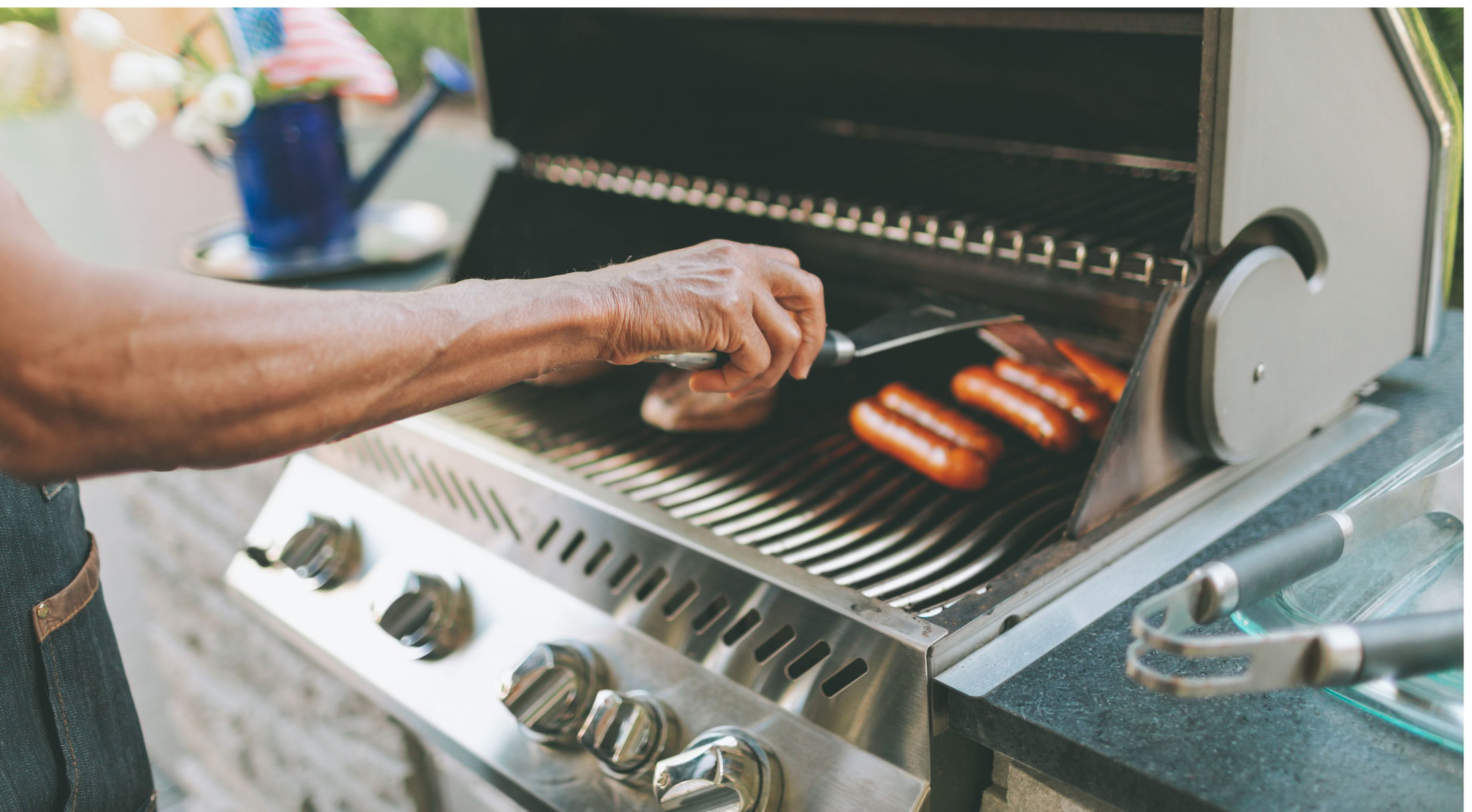 A person grilling sausages on a stainless steel barbecue grill.