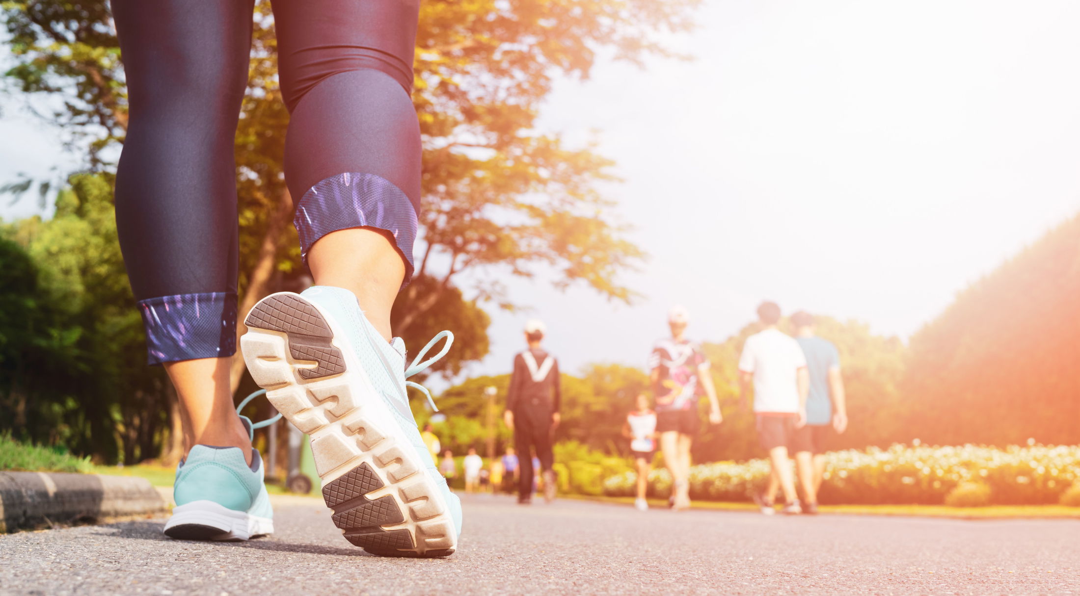 Close-up of a person walking on a sunny path in athletic shoes, surrounded by people and greenery.