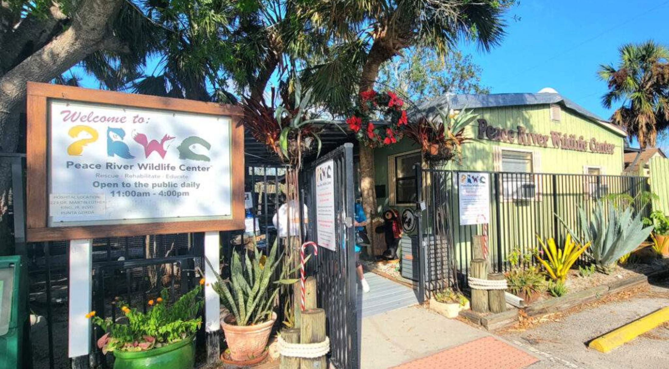 Entrance of Peace River Wildlife Center surrounded by lush plants and signage displaying visiting hours.
