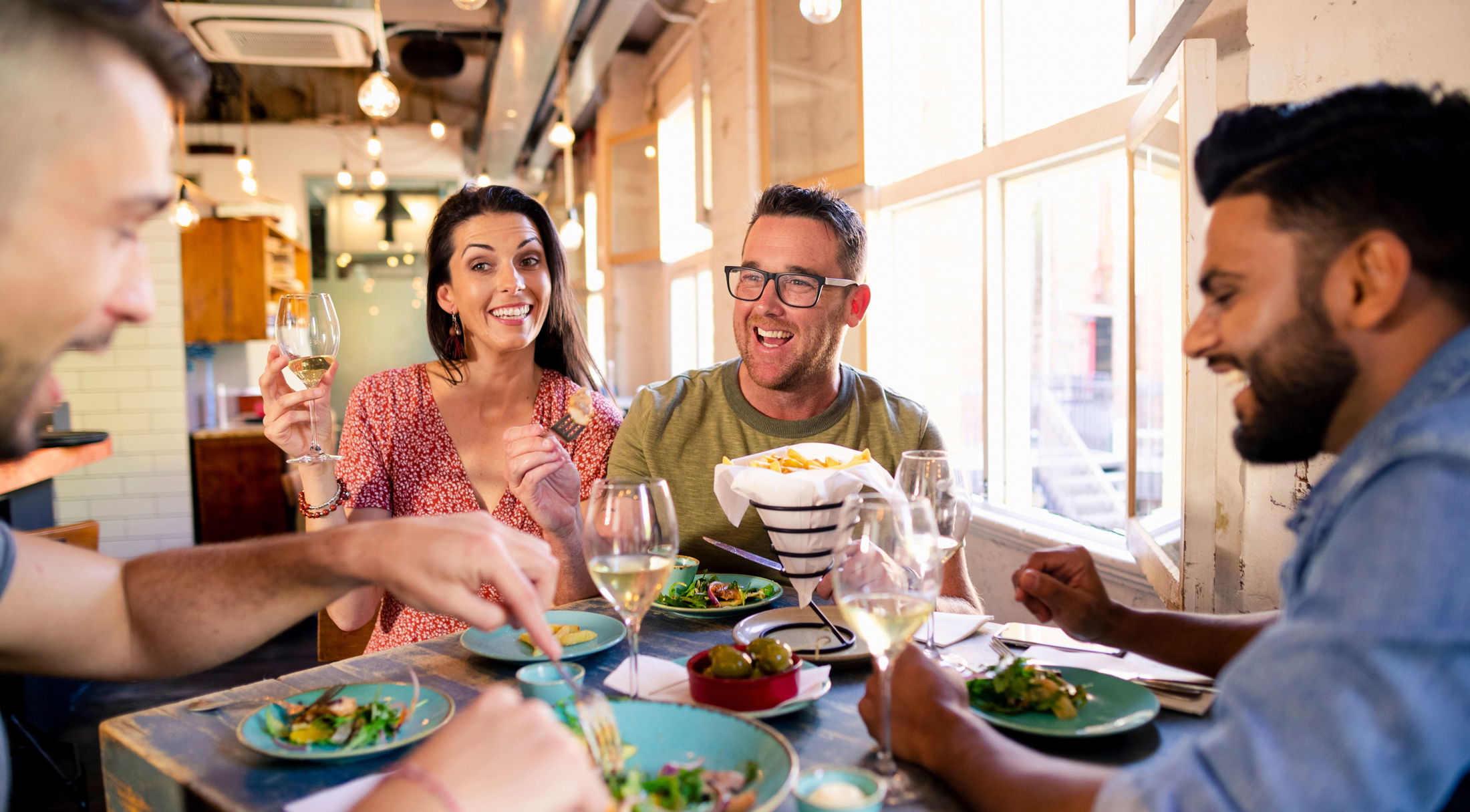 A group of friends enjoying a meal and wine together in a lively restaurant setting.