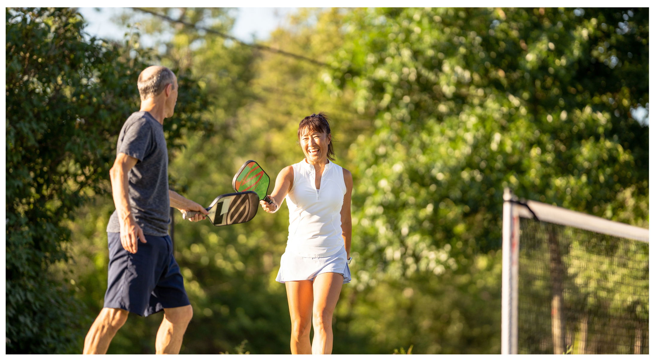 Two people playing pickleball outdoors, smiling and enjoying a sunny day.