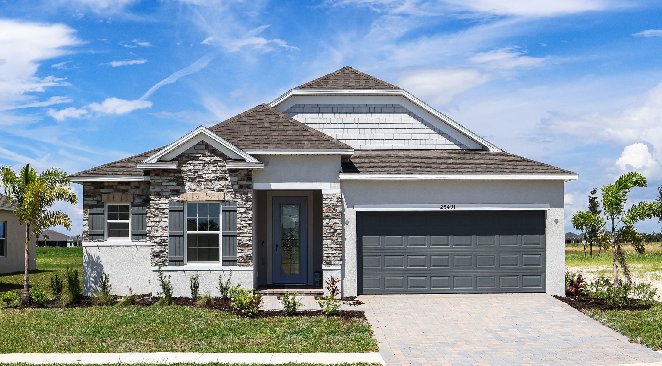 Modern single-story suburban house with stone accents, well-manicured lawn, and blue sky background.