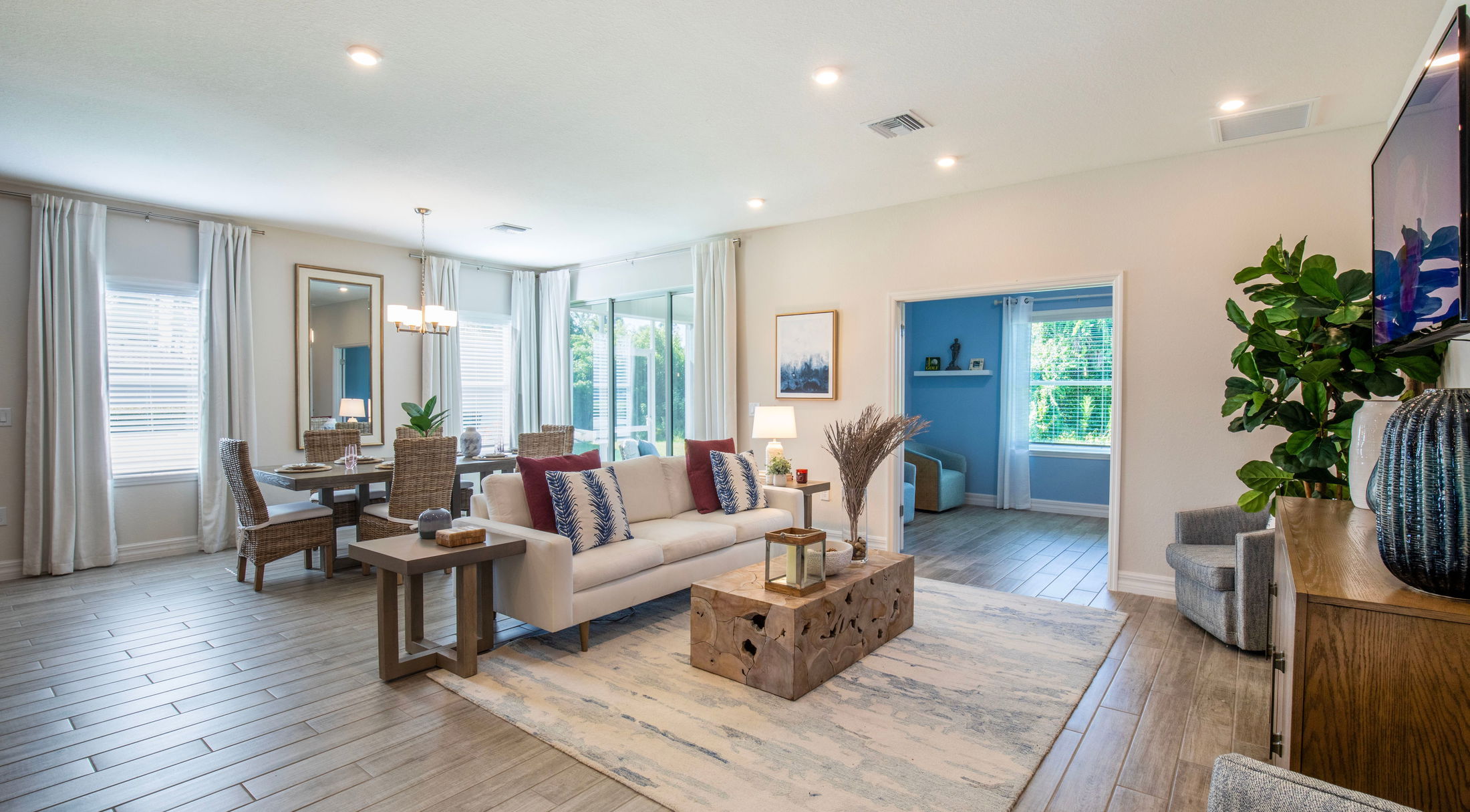 Modern open-plan living and dining room with natural light, featuring a beige sofa, wooden coffee table, and wicker dining chairs.