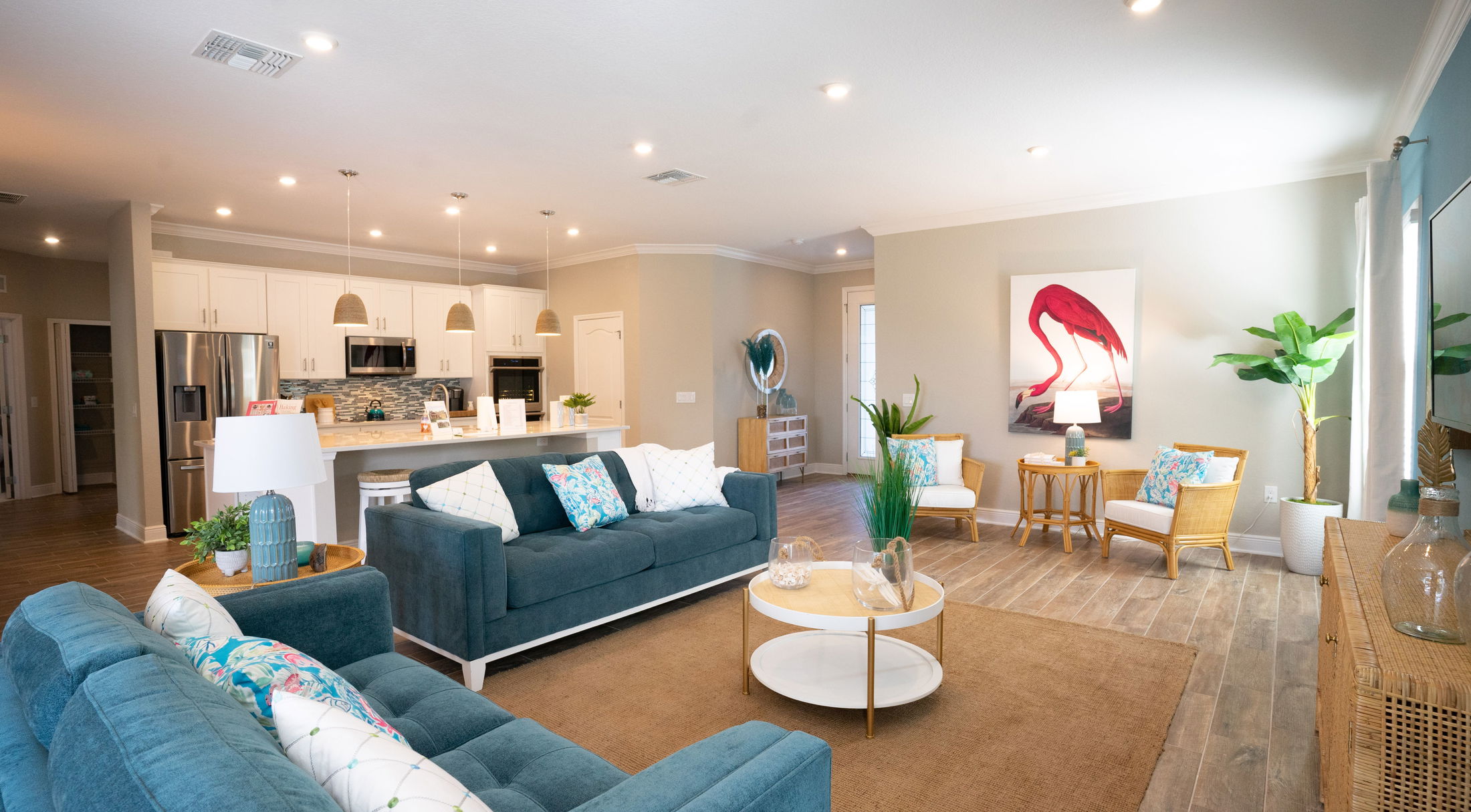 Modern open-concept living room and kitchen with blue sofas, wicker furniture, large artwork, and stylish decor.