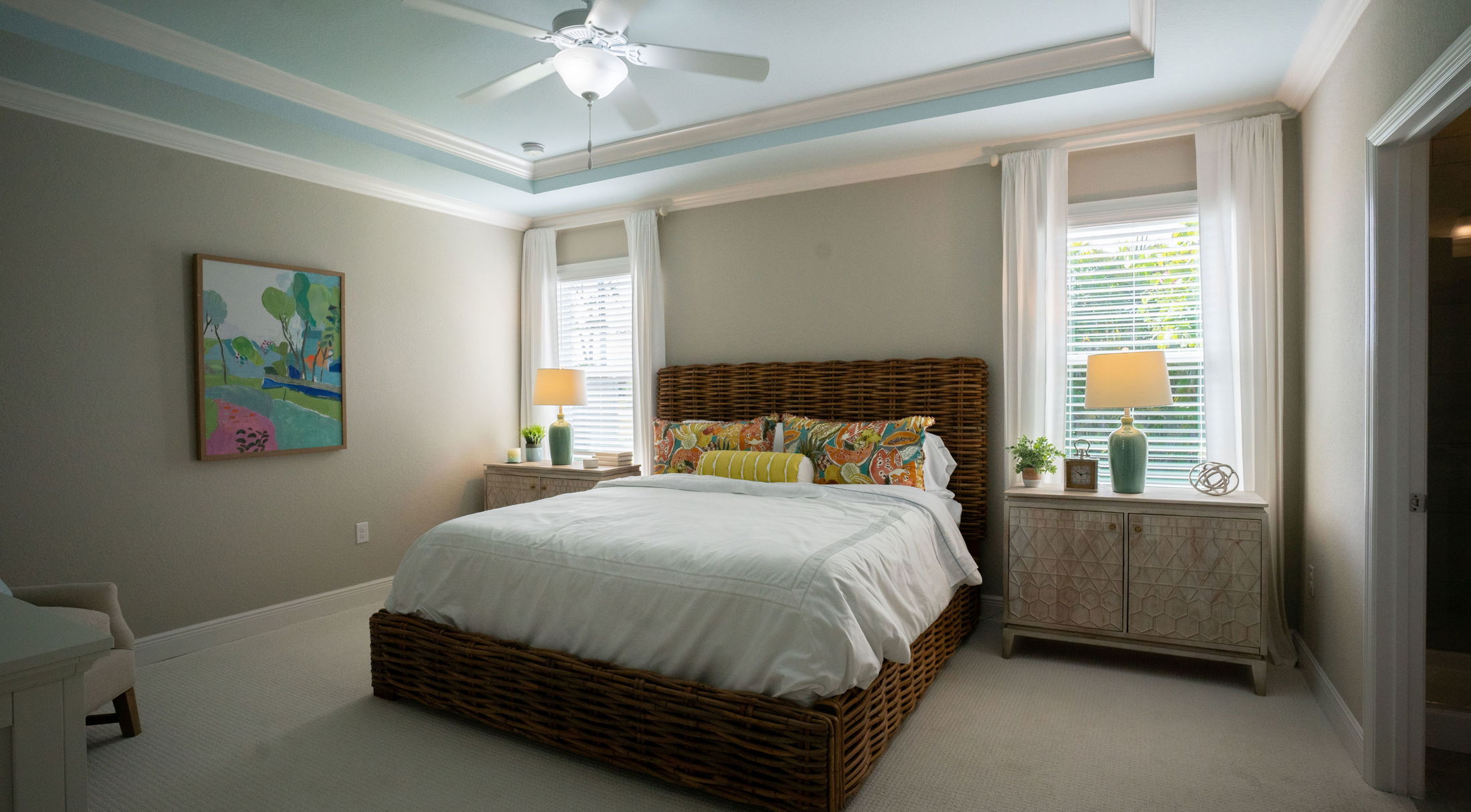 Modern bedroom with wicker bed, colorful pillows, and bright lamps on white nightstands.