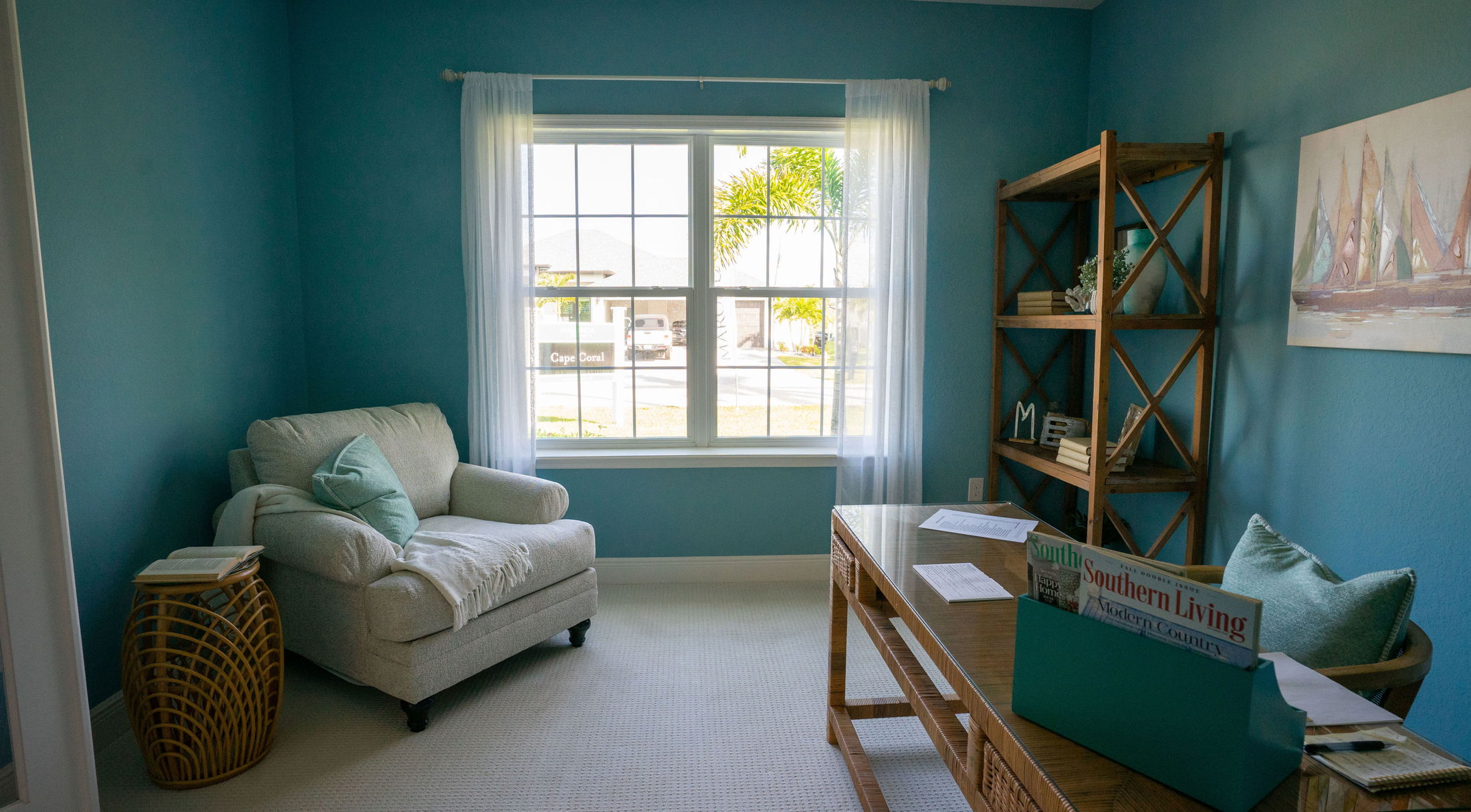 Cozy blue home office with natural light, featuring a plush armchair, wooden desk, and shelving unit.