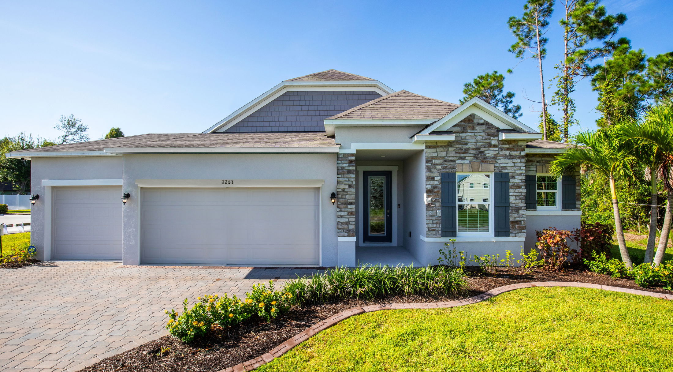 Modern single-story home with stone accents, double garage, and manicured landscaping under a clear blue sky.