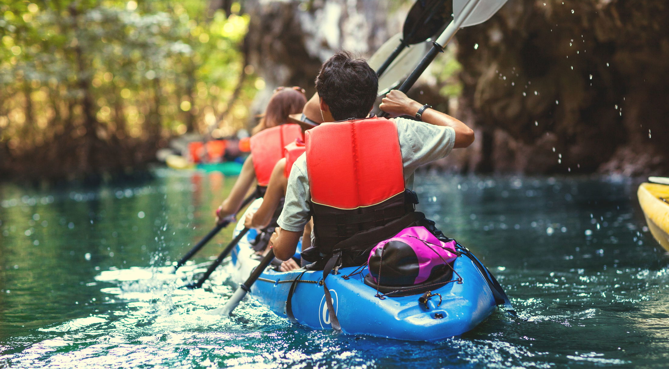 Two people kayaking through a scenic cave waterway while wearing life jackets.
