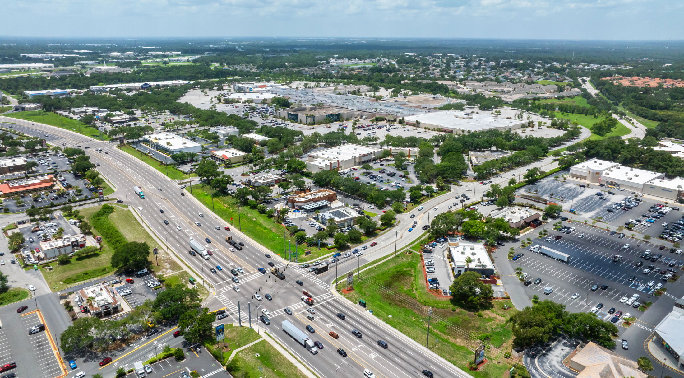 Aerial view of a busy urban intersection surrounded by commercial buildings and parking lots on a sunny day.
