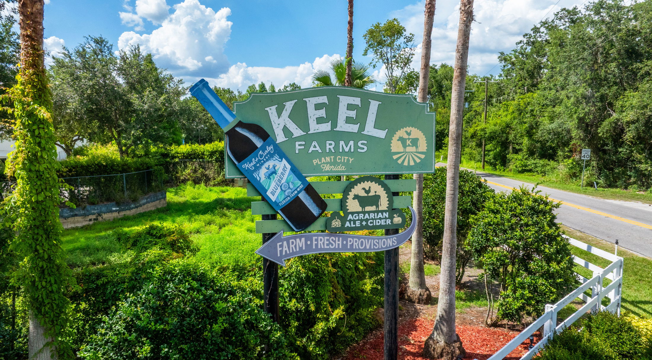 Sign for Keel Farms in Plant City, Florida, showcasing blueberry wine and agrarian ale and cider amid lush greenery.