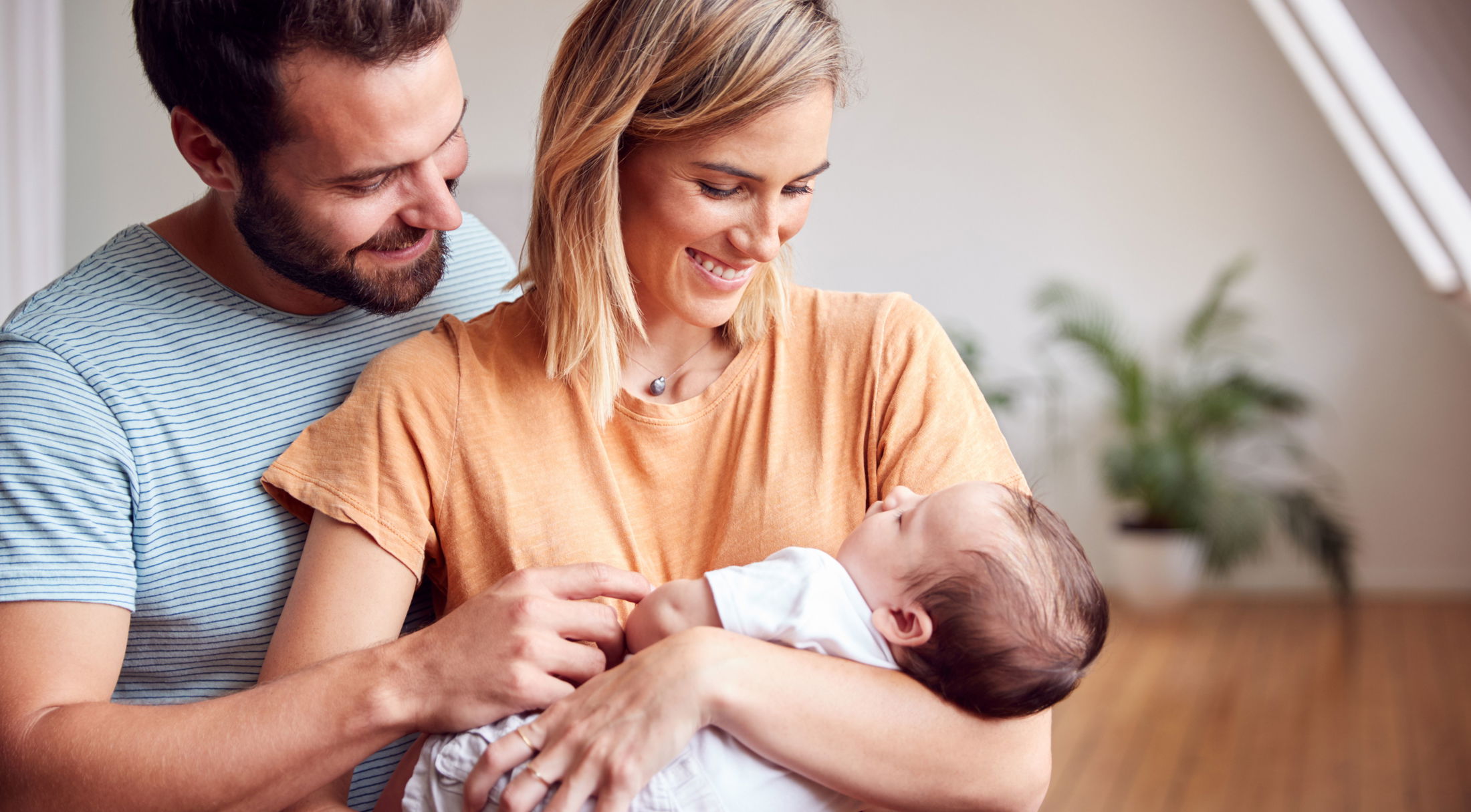 A happy couple lovingly gazing at their newborn baby indoors, surrounded by natural light and house plants.