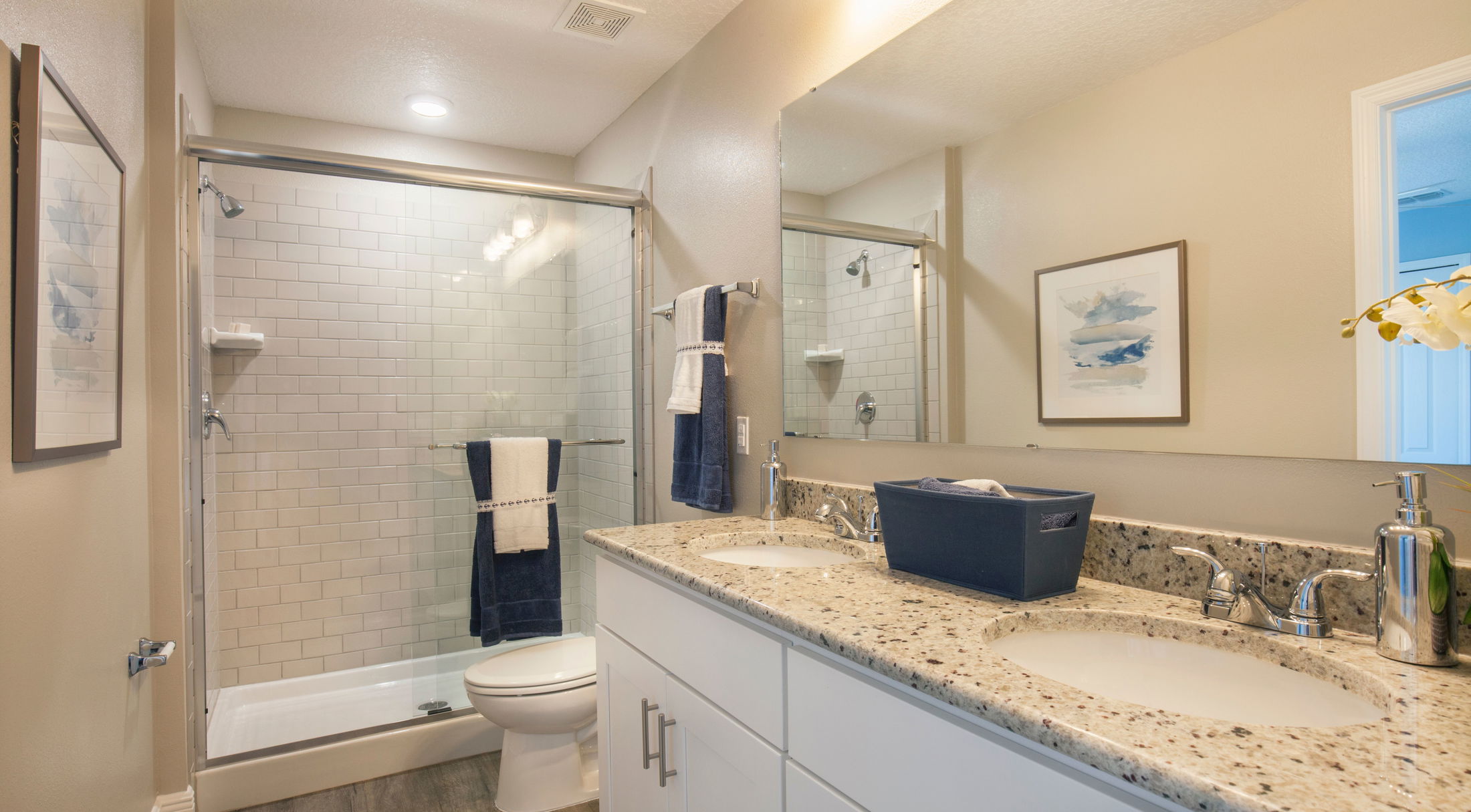 Modern bathroom with granite countertop, dual sinks, and a glass-enclosed shower featuring white subway tiles.