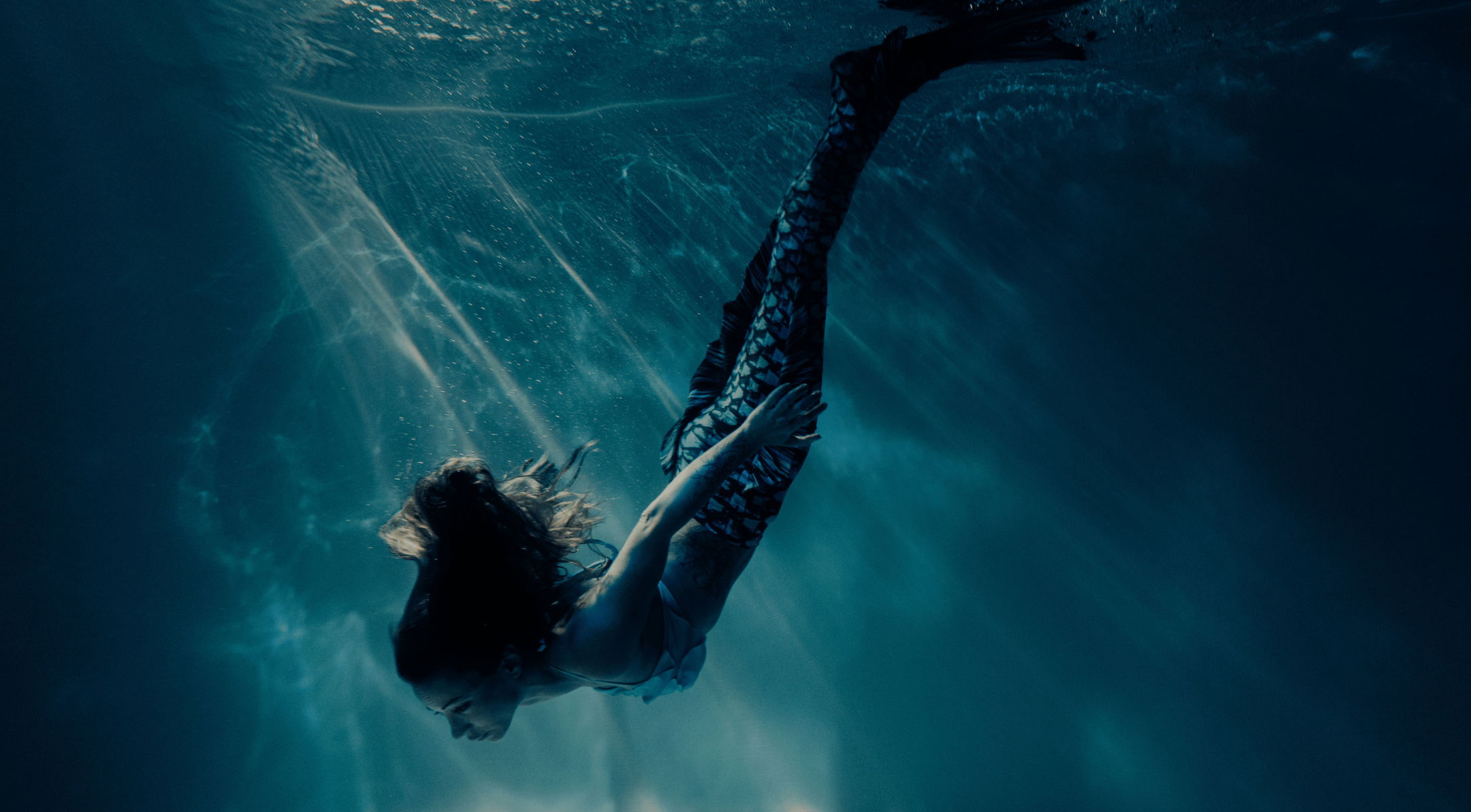 A mermaid gracefully swims underwater with rays of light filtering through the water.