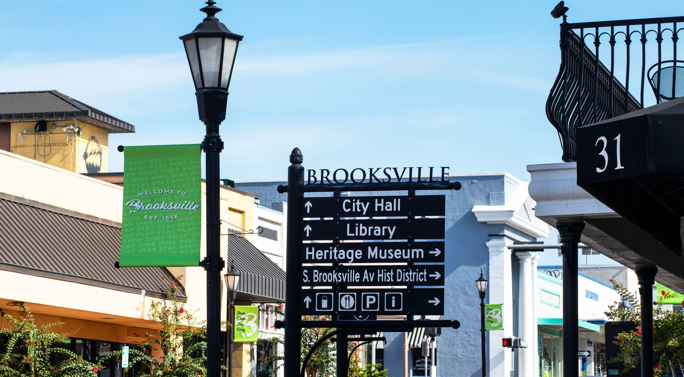 Street signs and banners welcome visitors to downtown Brooksville, highlighting city attractions like City Hall and the Heritage Museum.