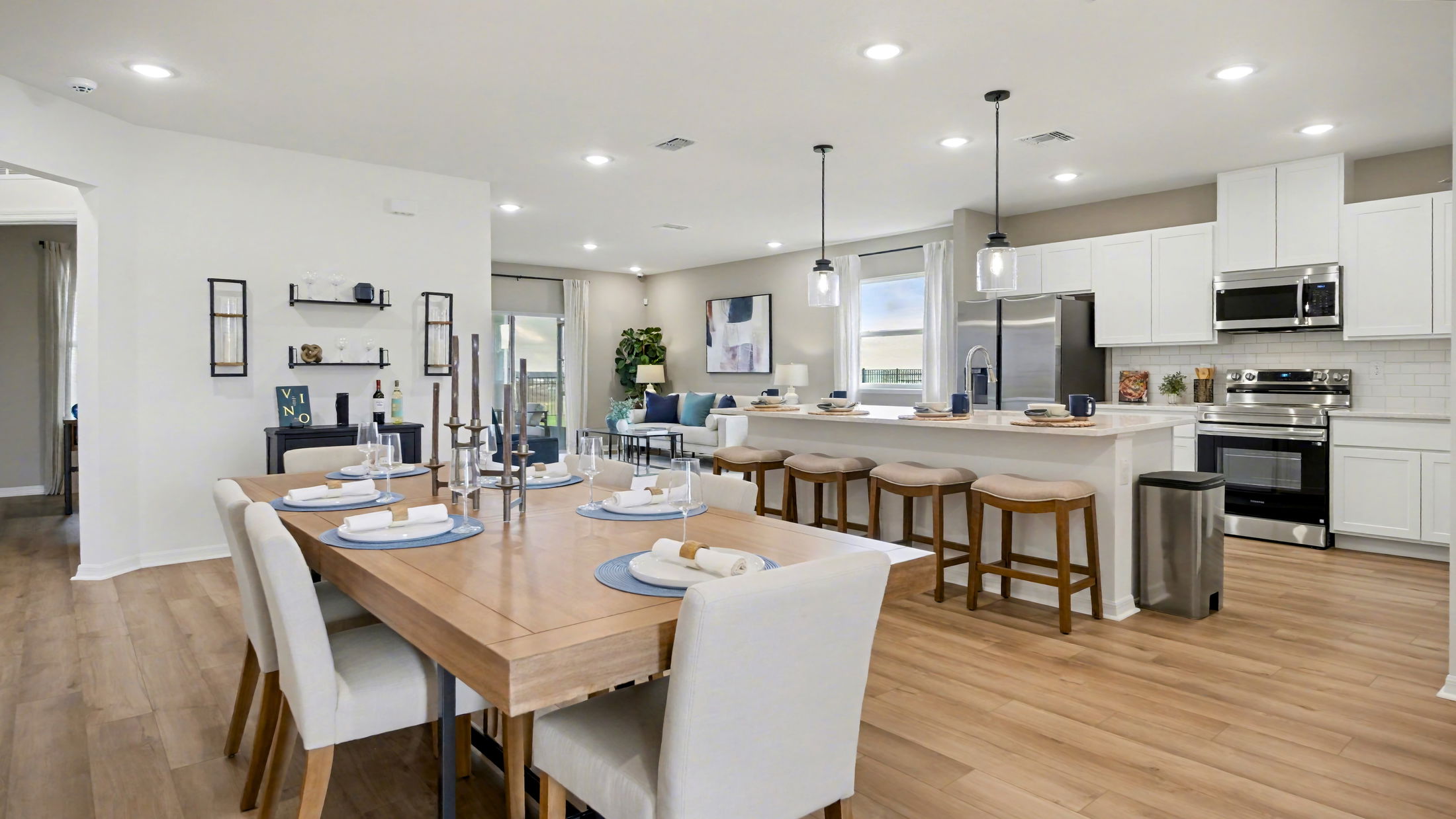 Modern open-concept kitchen and dining area featuring elegant white cabinetry, stainless steel appliances, and a wooden dining table with place settings.