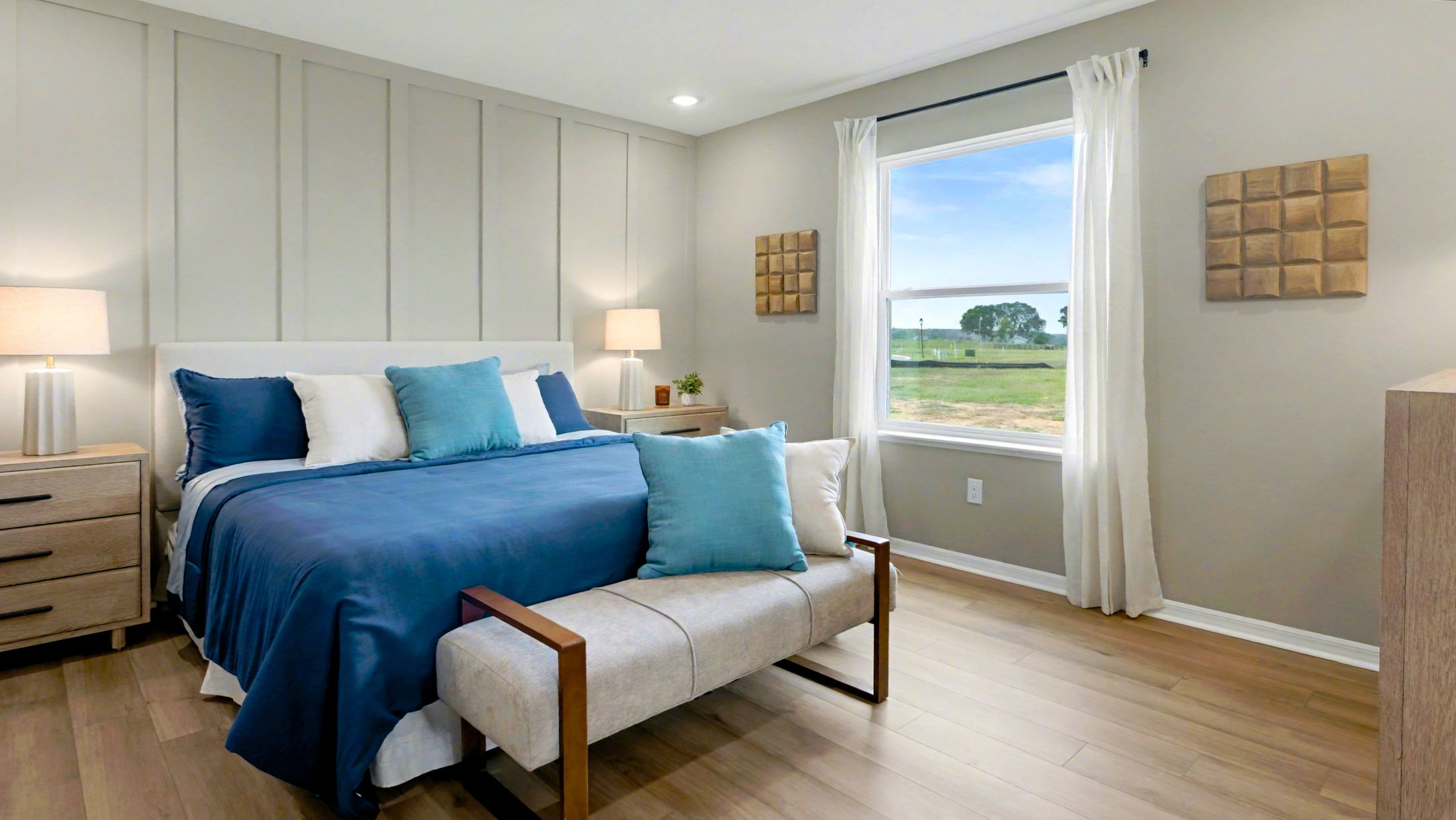 Modern bedroom with a blue-themed bedding set, wooden floor, beige walls, and a window overlooking a green landscape.