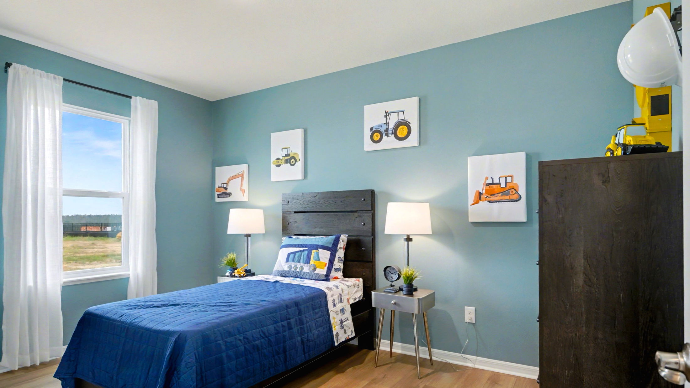 Bright and inviting child's bedroom with a blue theme, featuring construction vehicle decor, a single bed, and natural light from a large window.
