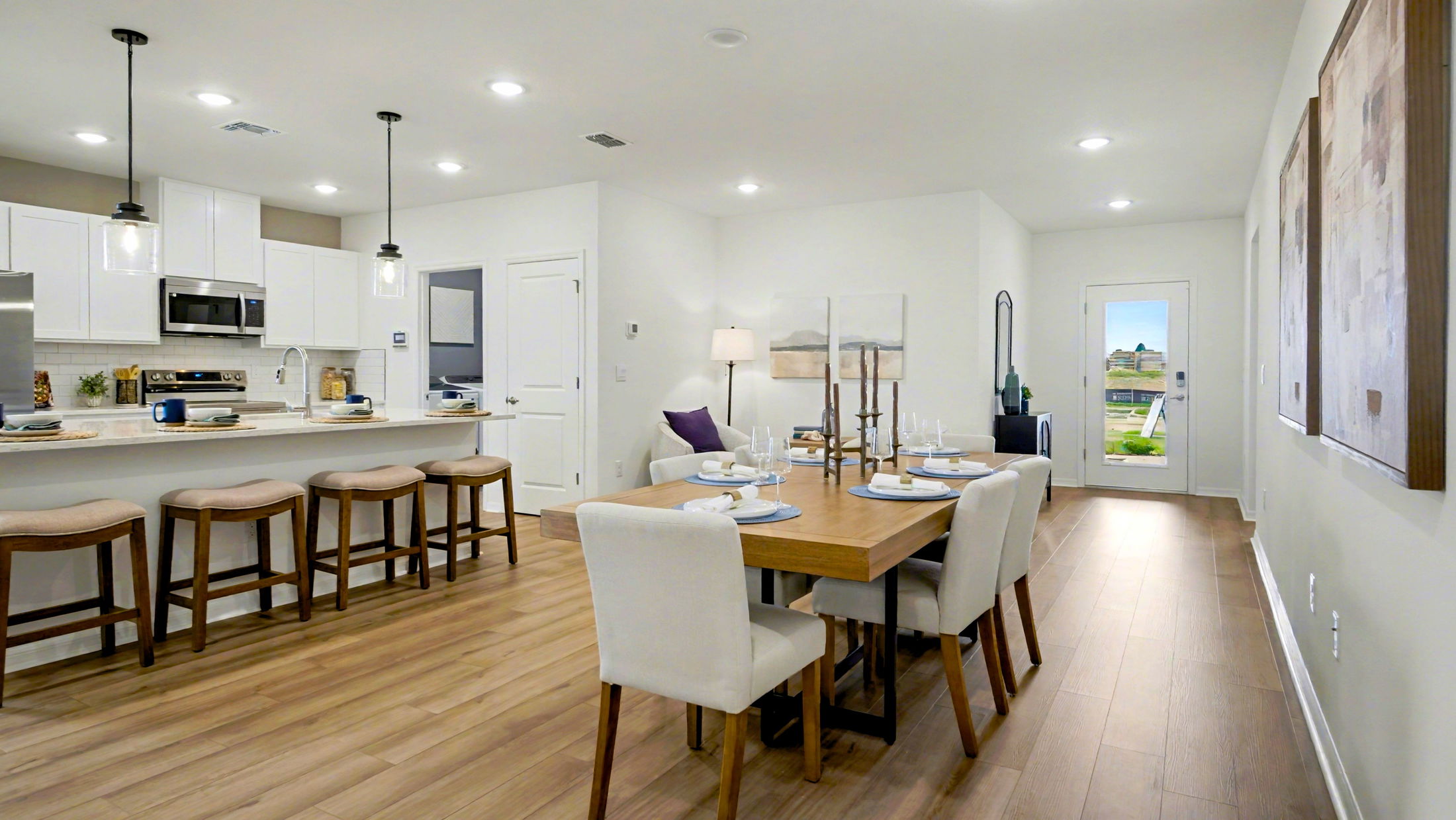 Modern open-concept kitchen and dining area with white cabinetry, wooden flooring, contemporary lighting, and a set dining table.