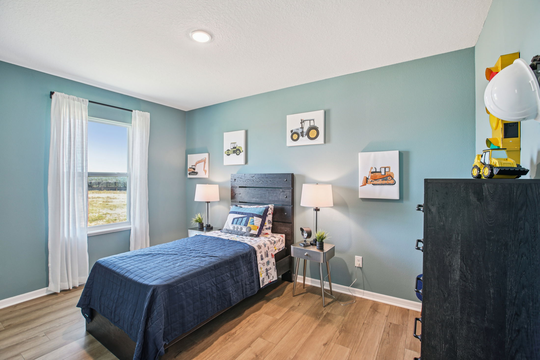 Cozy children's bedroom featuring a navy quilt, construction-themed wall art, and modern furnishings with natural light.
