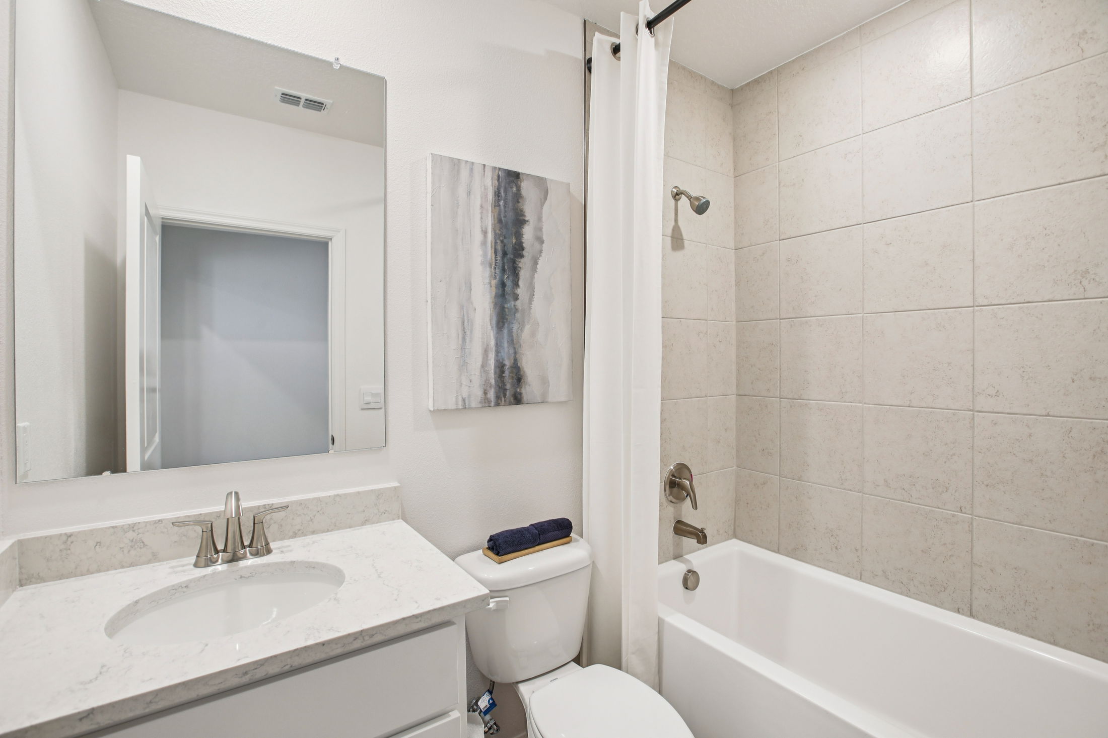 Modern bathroom featuring a marble vanity, a bathtub with a shower, and artistic wall decor.