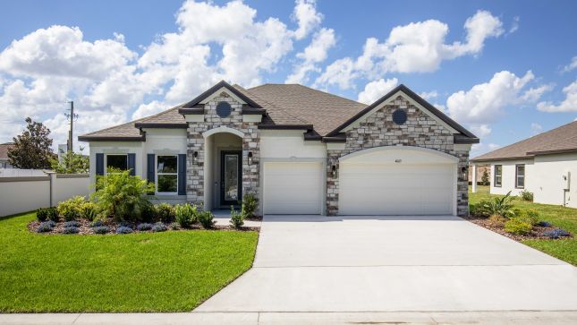 Modern single-story suburban home with stone accents, a two-car garage, and landscaped front yard under a clear blue sky.