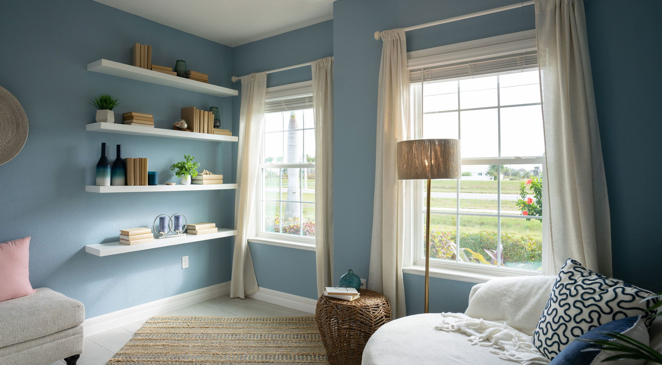 Cozy blue reading nook with floating shelves, comfy furniture, and a large window offering natural light.