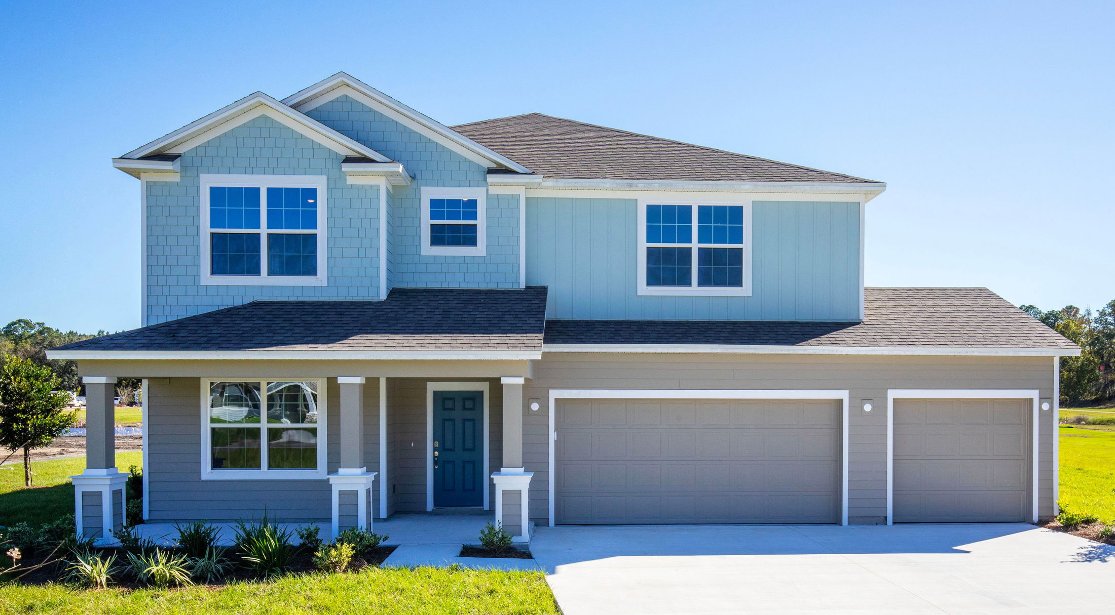 Modern two-story suburban home with blue siding, a covered porch, and a three-car garage under a clear blue sky.