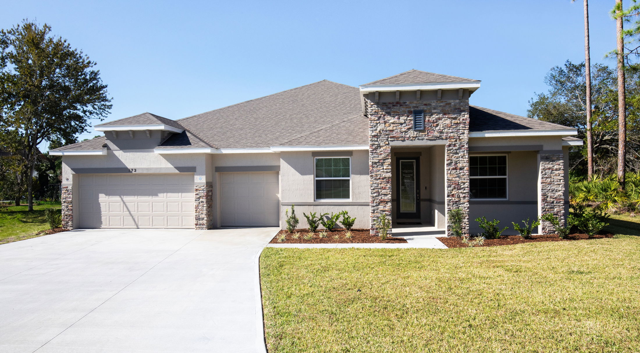 Modern single-story home with stone accents, double garage, and well-maintained front lawn under a clear blue sky.