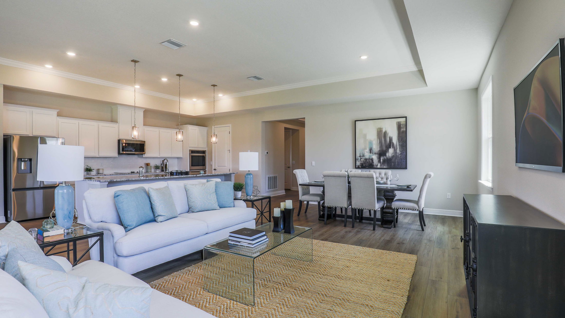 Spacious modern living room and kitchen with elegant decor, featuring a cozy white sofa, glass coffee table, and breakfast bar with pendant lighting.