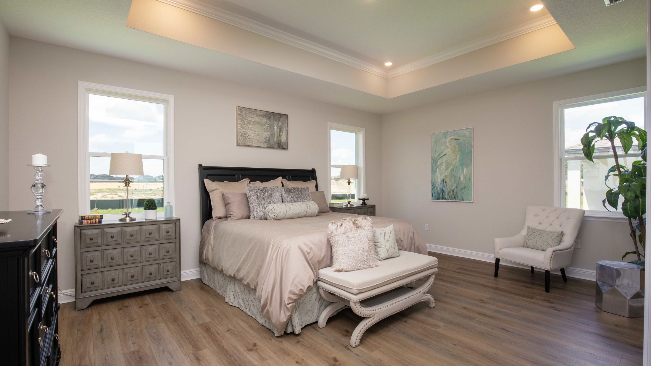 Modern bedroom with elegant decor, featuring a cozy bed, stylish nightstands, ambient lighting, framed artwork, and a plush armchair on a wooden floor.